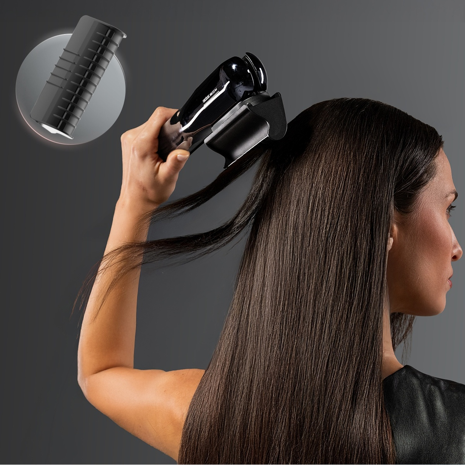 Una donna usa una piastra per capelli nera sui suoi lunghi capelli castani su sfondo grigio.