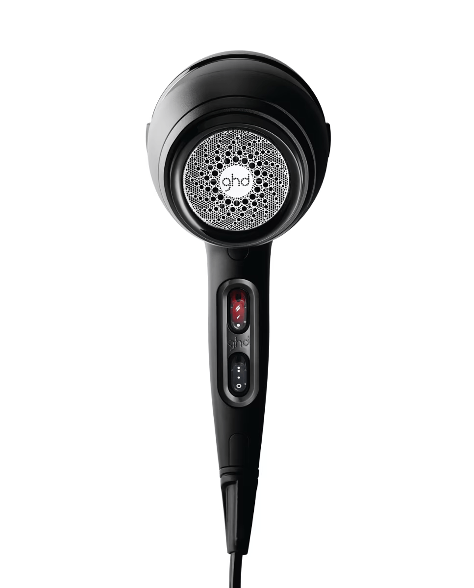 Un secador de pelo ghd negro con rejilla plateada y controles rojos sobre fondo blanco.