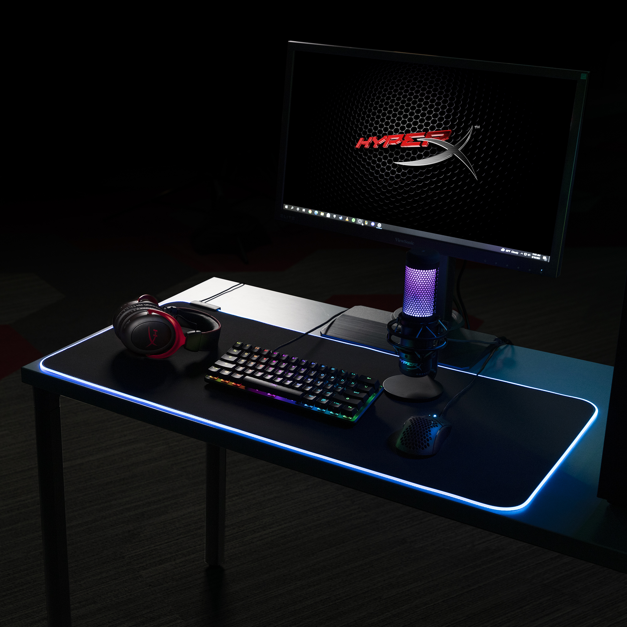 Monitör, arkadan aydınlatmalı klavye, fare, kulaklık ve RGB ışıklı mikrofona sahip bir oyun masası.
