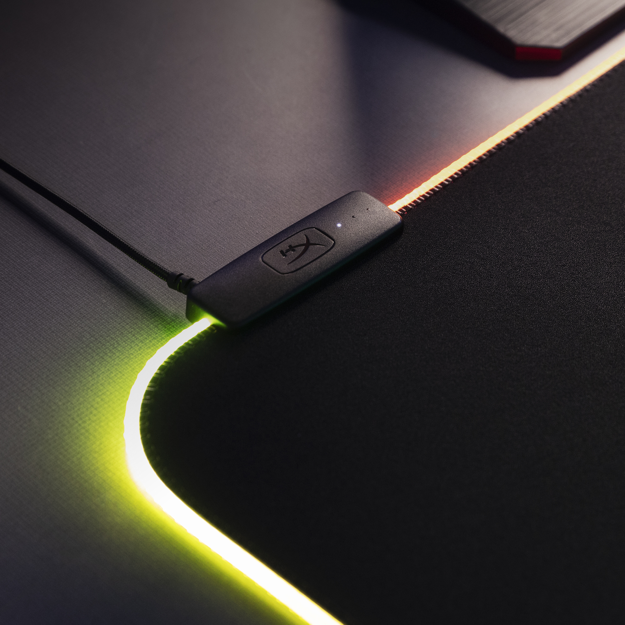 Kenarında parlak RGB aydınlatma ve küçük bir kontrol ünitesi olan siyah mousepad.