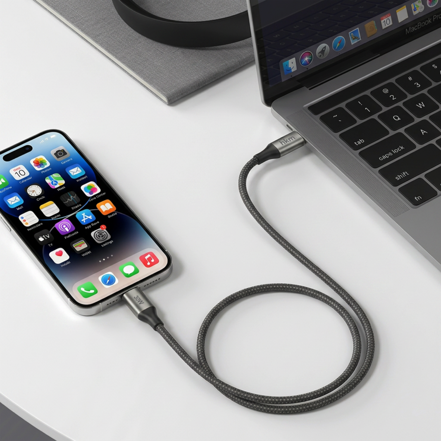 Beyaz bir masada bir dizüstü bilgisayara USB kabloyla bağlı gri bir akıllı telefon.