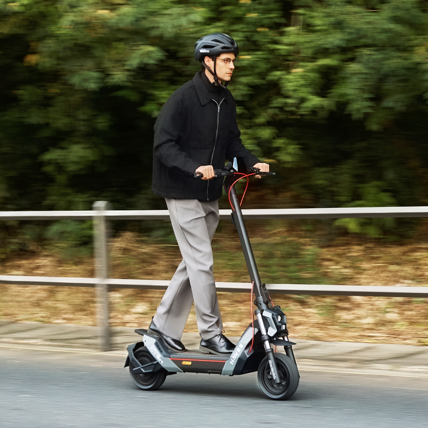 Un uomo con il casco guida un monopattino elettrico su una strada davanti a cespugli verdi.