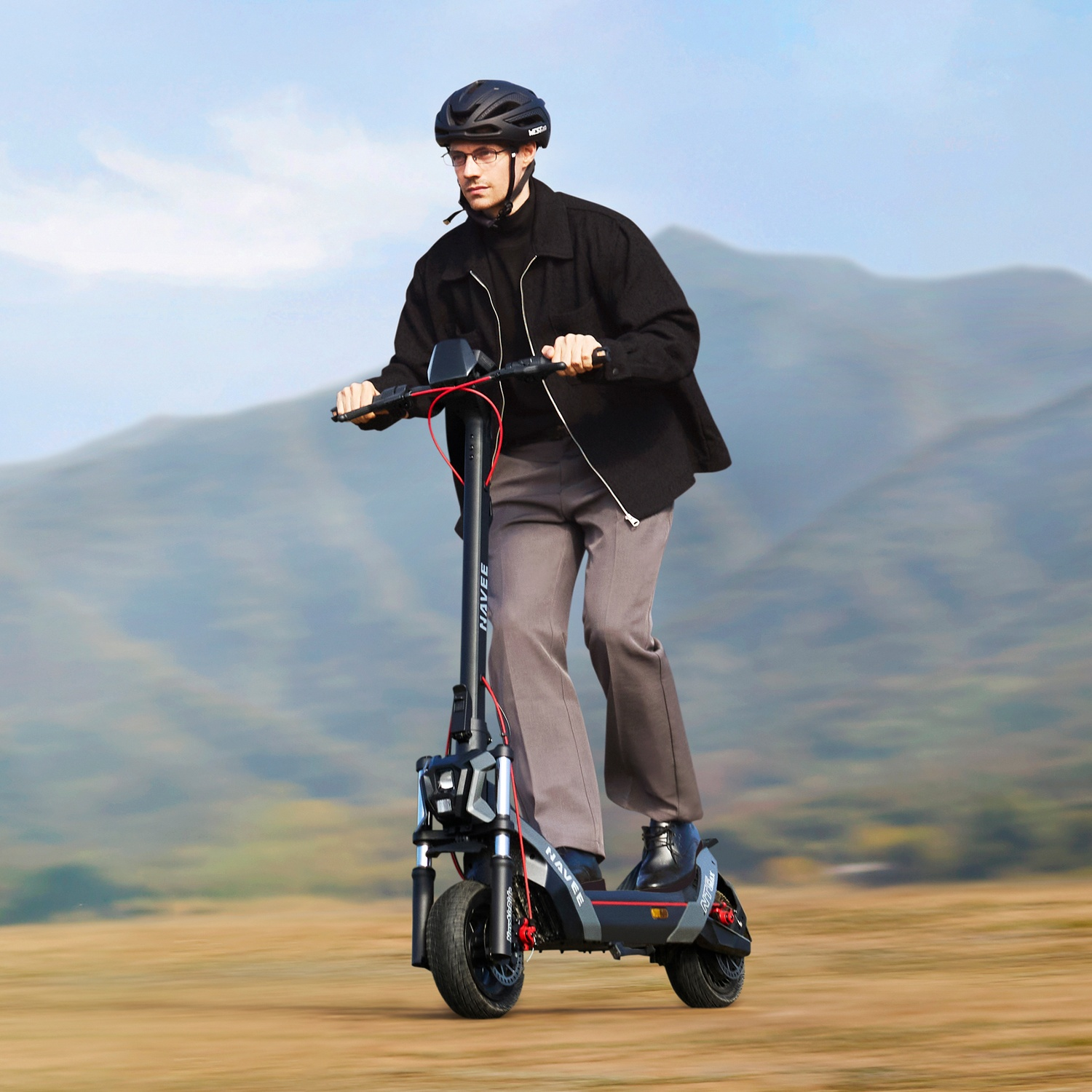 Un uomo con casco guida un monopattino elettrico nero davanti a uno sfondo montuoso.