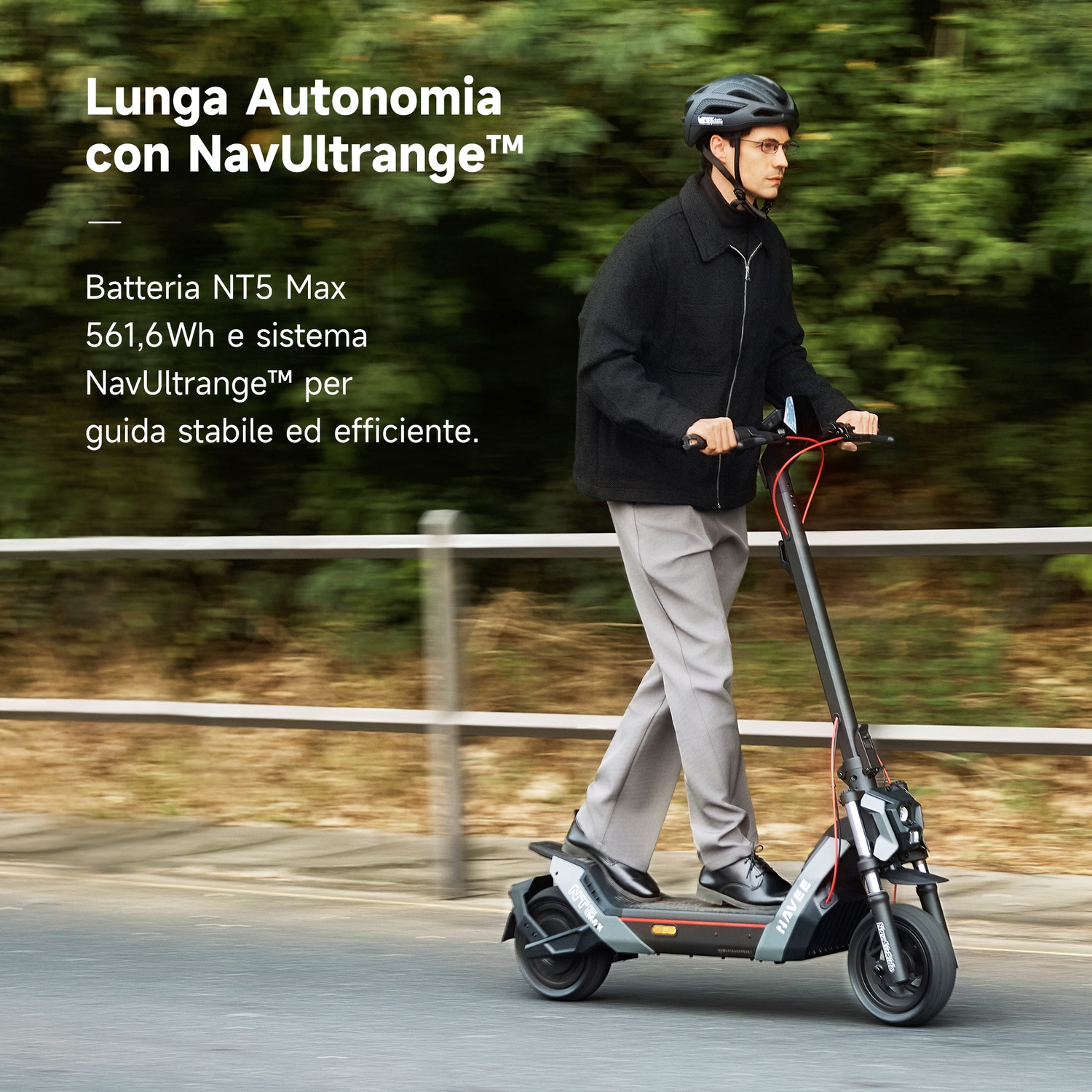 Un uomo con casco guida un monopattino elettrico vicino a un guardrail e alberi.