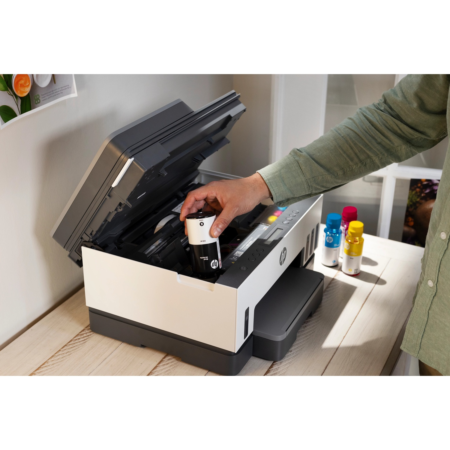 A person refills ink into an open white and gray HP printer on a wooden table.