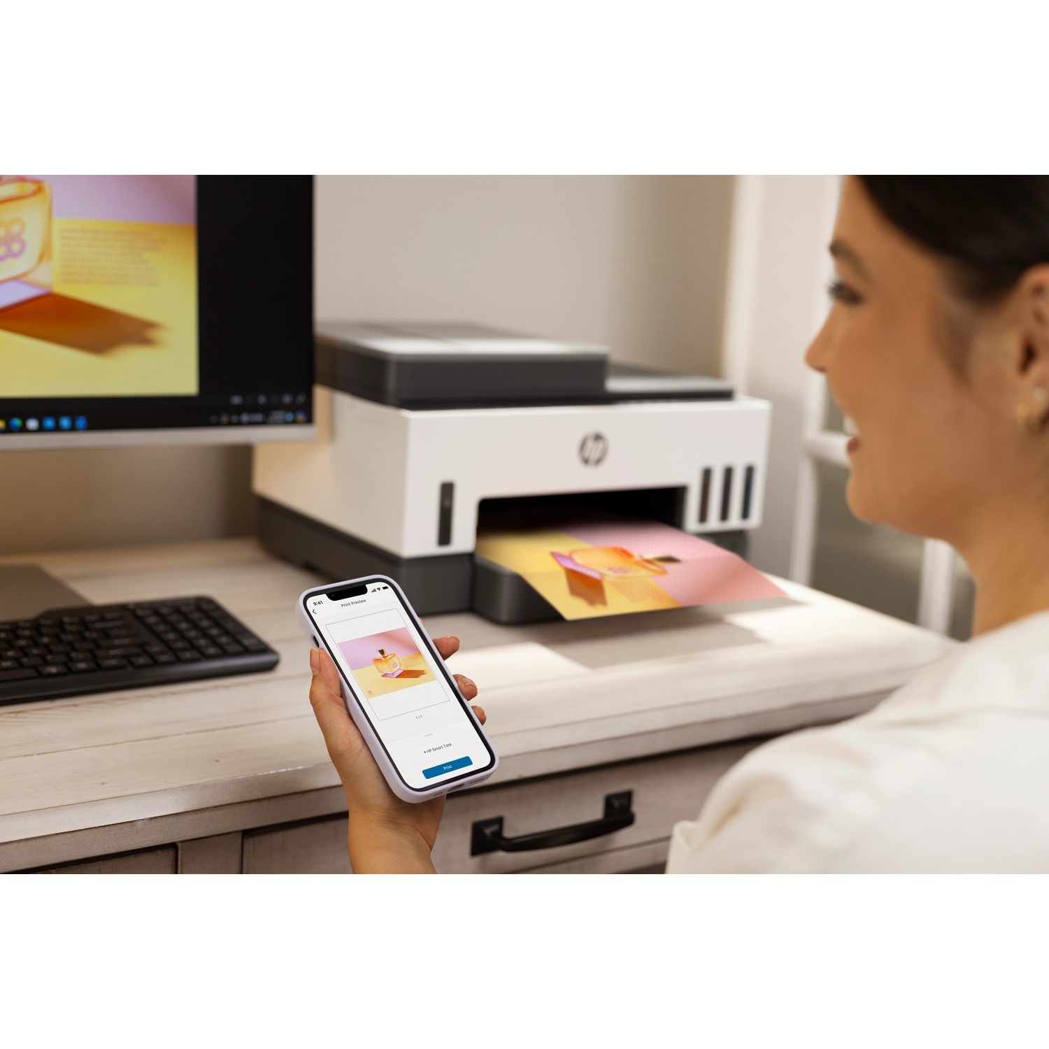 A woman holds a smartphone showing a print preview while a printer in the background prints a picture.