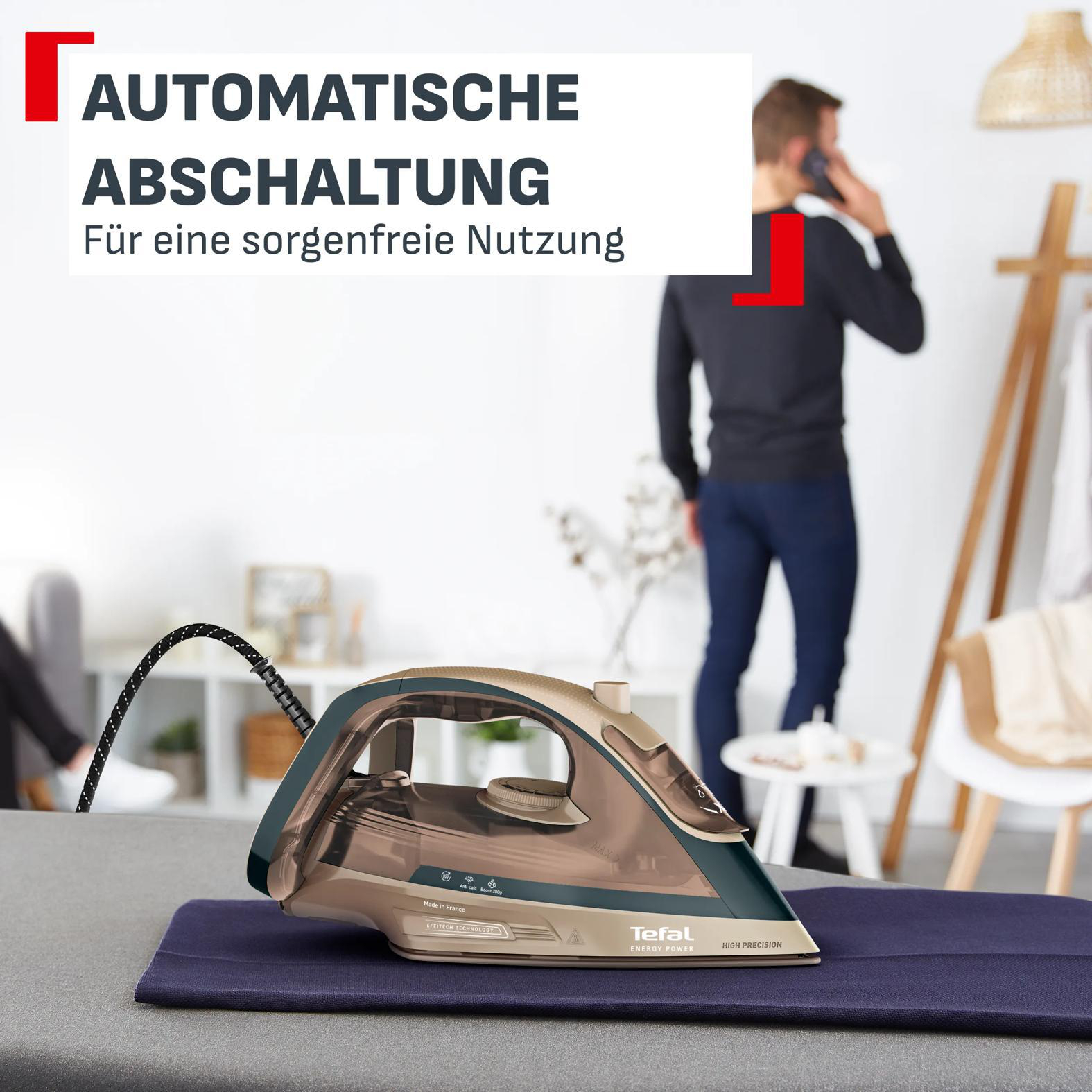Ein Tefal-Bügeleisen steht auf einem Tisch in einem Raum mit einem Mann im Hintergrund.