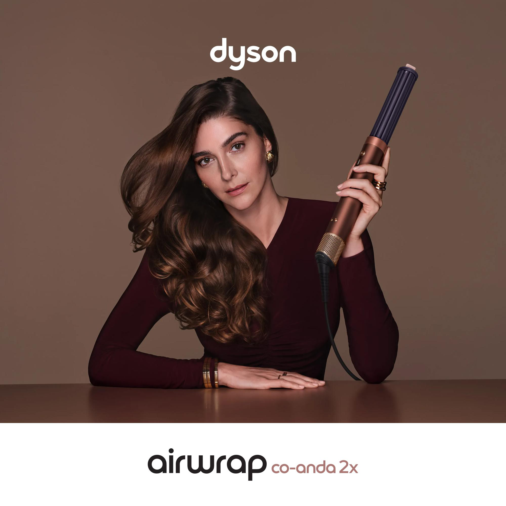 Eine Frau hält einen Dyson Airwrap vor einem braunen Hintergrund mit Text.