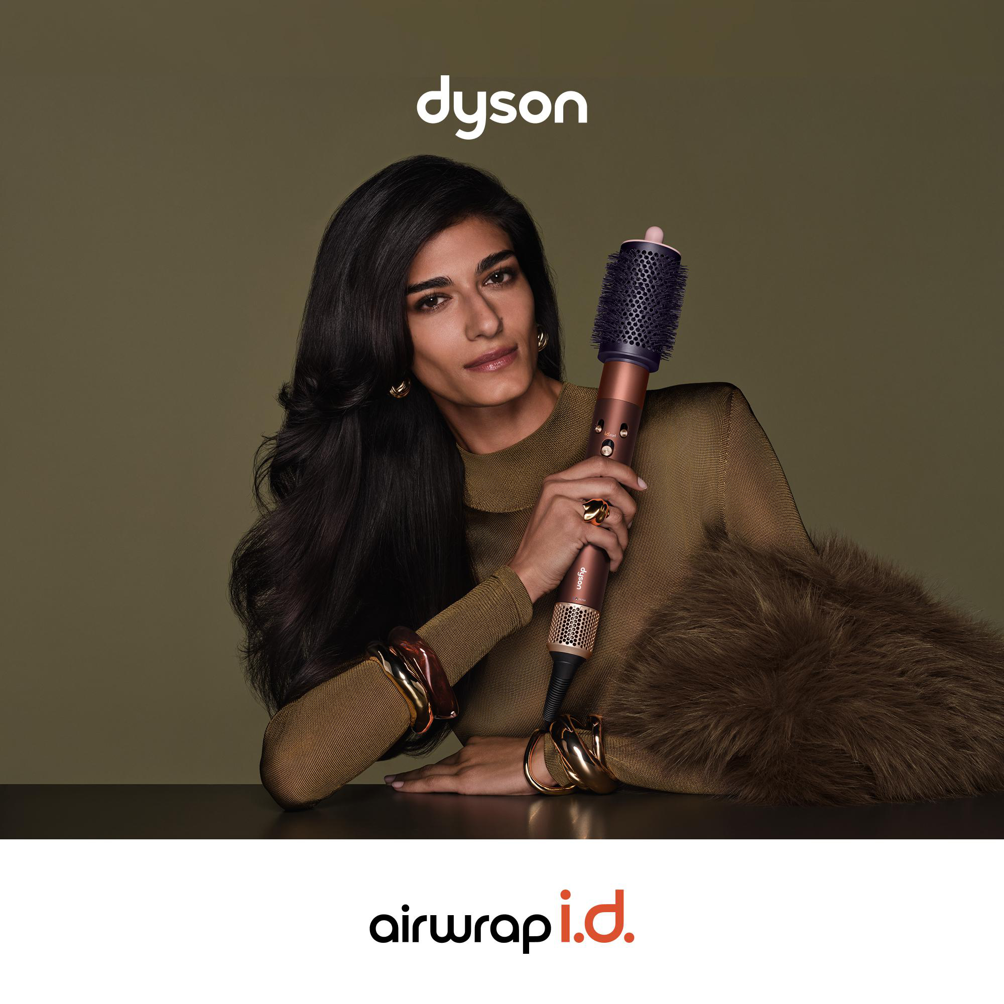 Eine Frau hält einen Dyson Airwrap i.d. vor olivgrünem Hintergrund, der Markenname steht oben und unten.