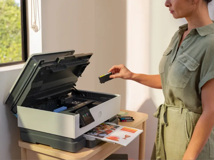 Eine Frau in einem grünen Kleid wechselt die Tintenpatrone in einem modernen Drucker auf einem Holztisch.