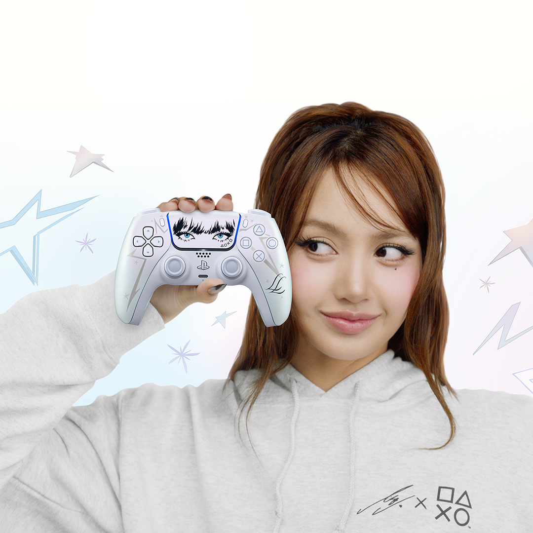 Eine Frau in einem hellen Kapuzenpulli hält einen weißen PlayStation-Controller mit grafischem Augenmotiv in der Hand.