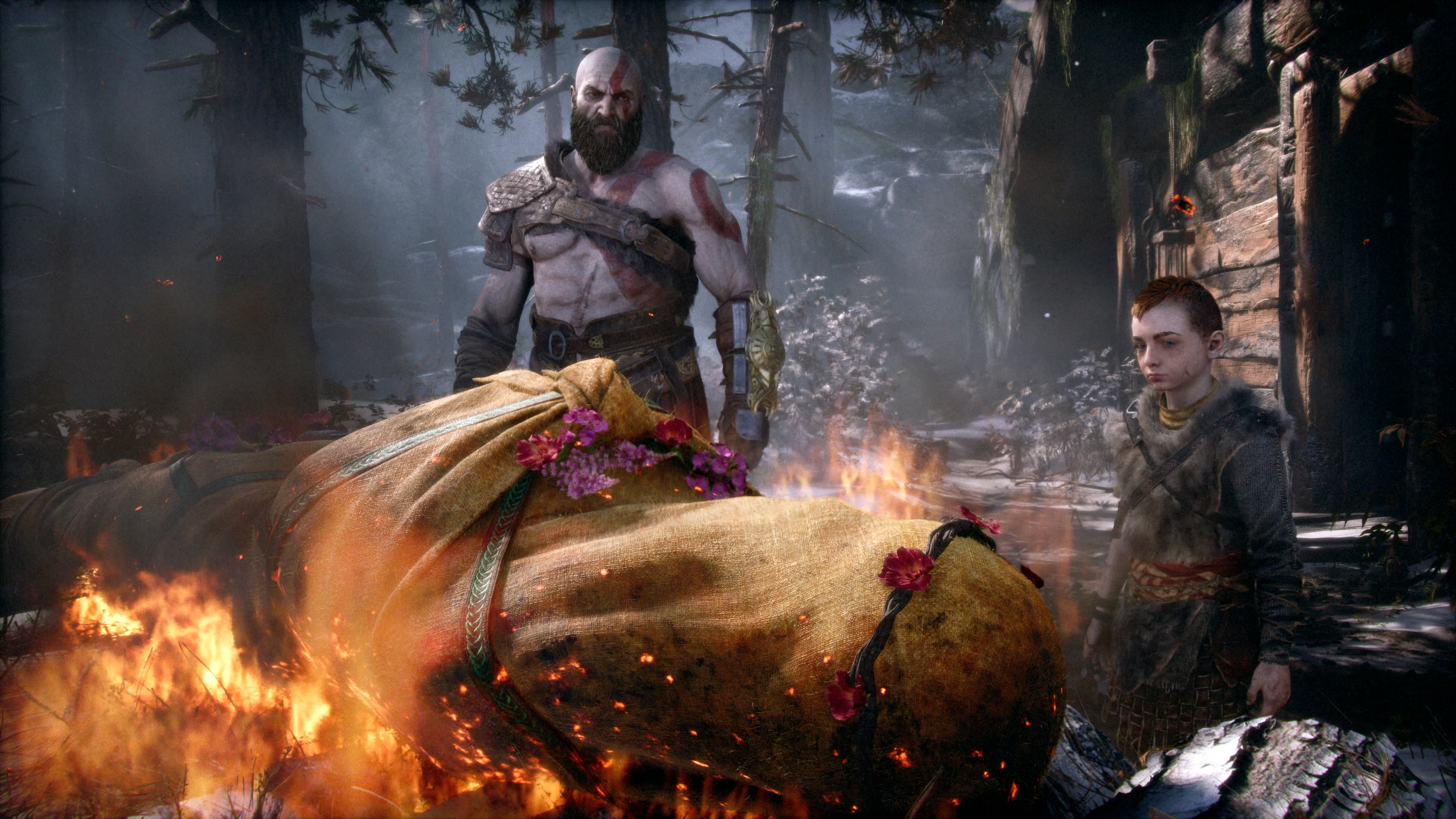 Kratos und Atreus stehen neben einer brennenden Leiche, die in gelbes Tuch gewickelt und mit Blumen geschmückt ist.