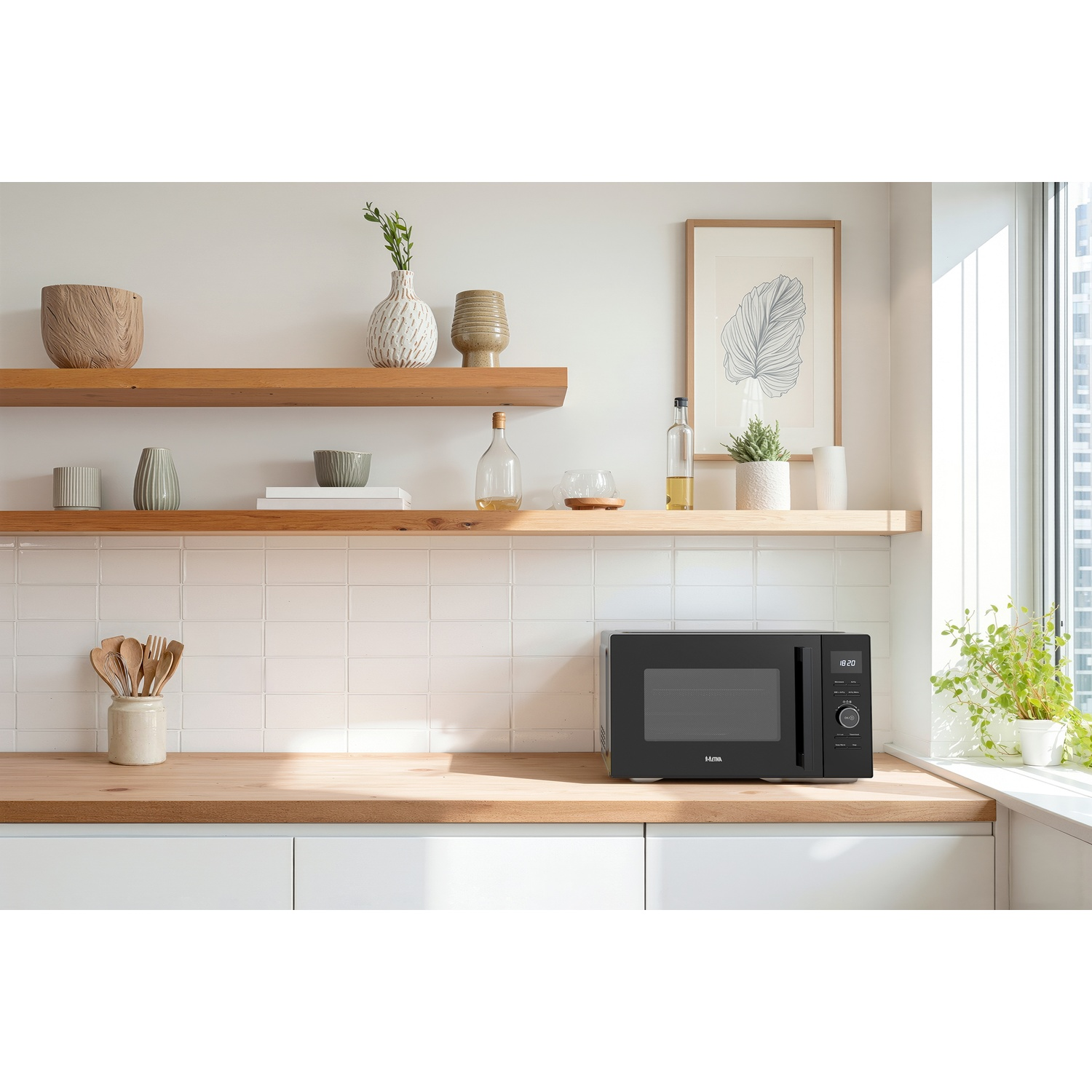 A black microwave sits on a wooden kitchen counter below shelves with vases, plants, and framed art.
