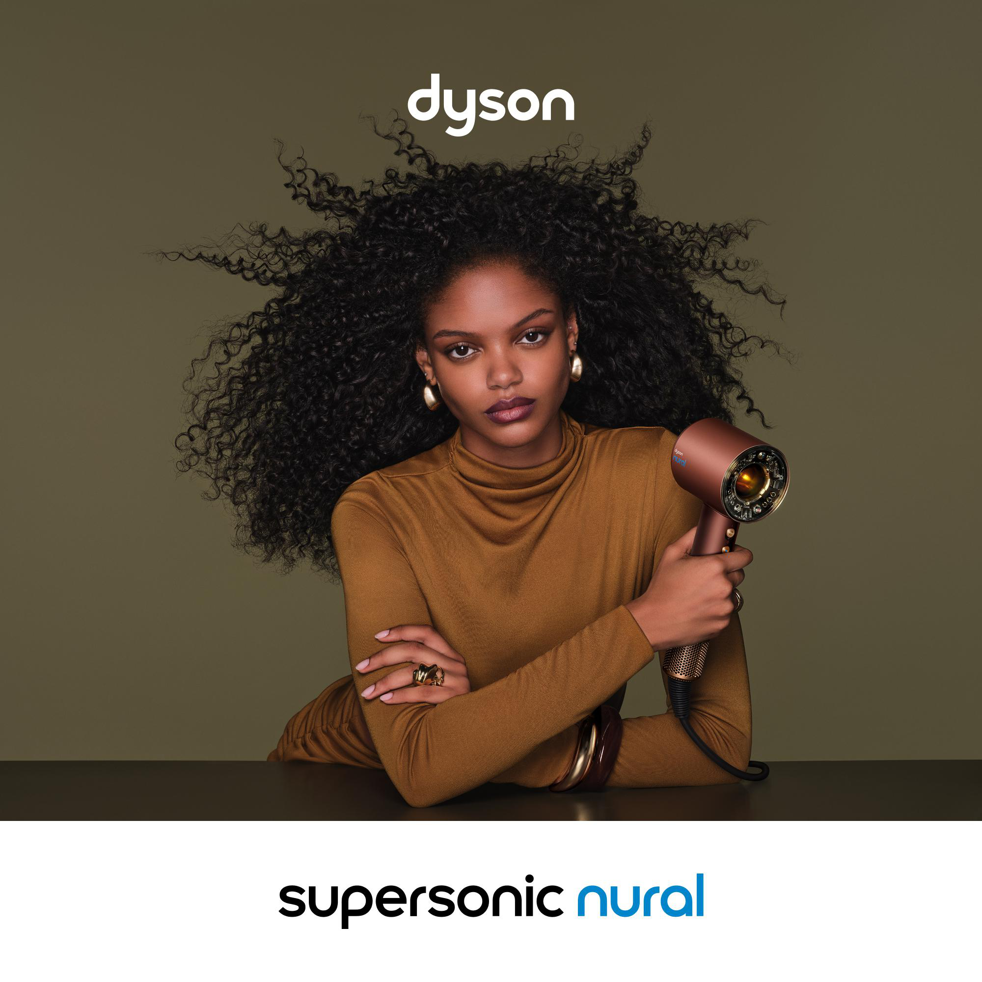 Eine Frau mit voluminösen Locken hält einen kupferfarbenen Dyson Supersonic nural Haartrockner.