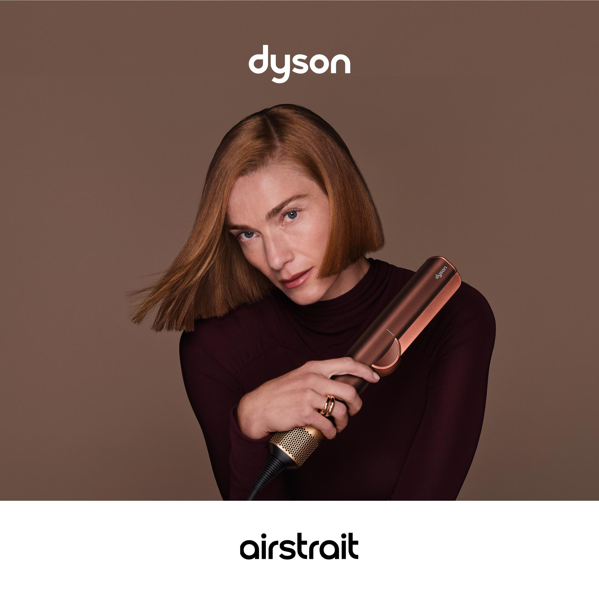 Eine Frau hält einen braunen Dyson Airstrait Haarglätter vor braunem Hintergrund mit Dyson-Logo.