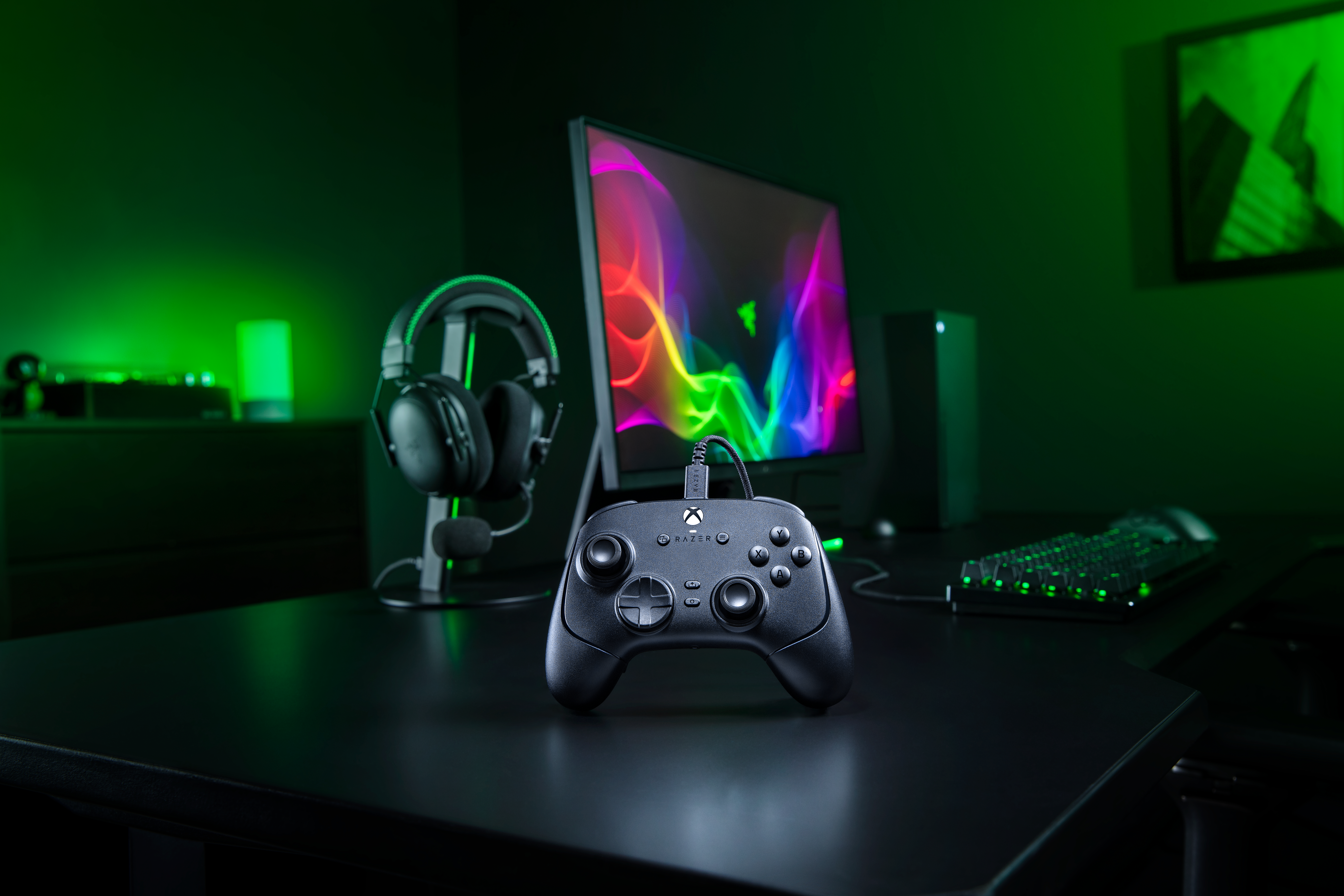 Ein schwarzer Xbox-Controller auf einem Schreibtisch in einem Raum mit grünem Licht, Monitor und Headset.