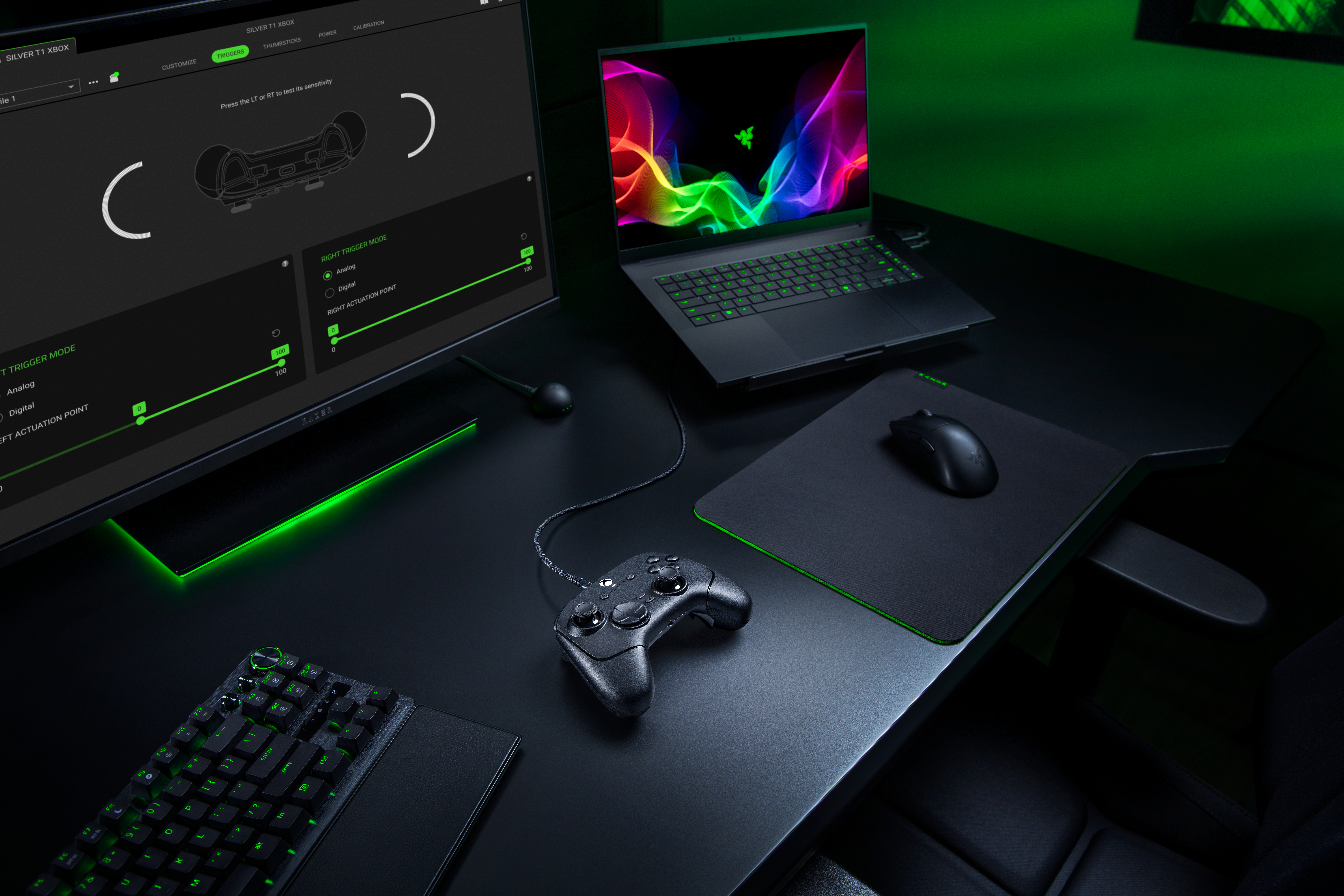 Ein Gaming-Schreibtisch mit Laptop, Monitor, Controller, Maus und Tastatur, beleuchtet in Grün.