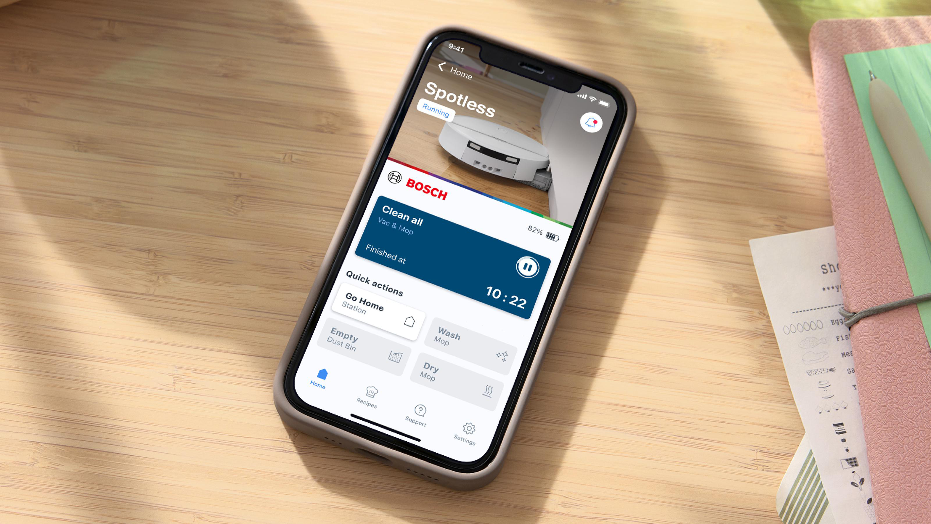 Ein Smartphone auf einem Holzisch zeigt eine Bosch-App zur Steuerung eines Staubsaugerroboters.