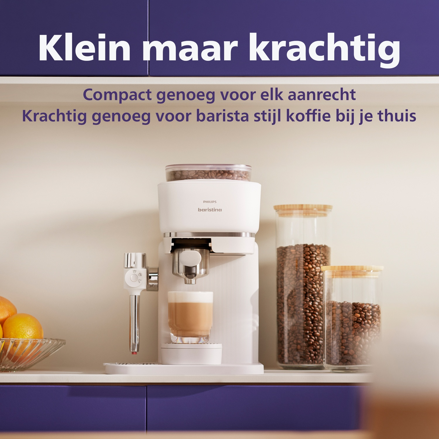 A white Philips Baristina coffee machine with a glass of cappuccino, jars of coffee beans, and oranges.