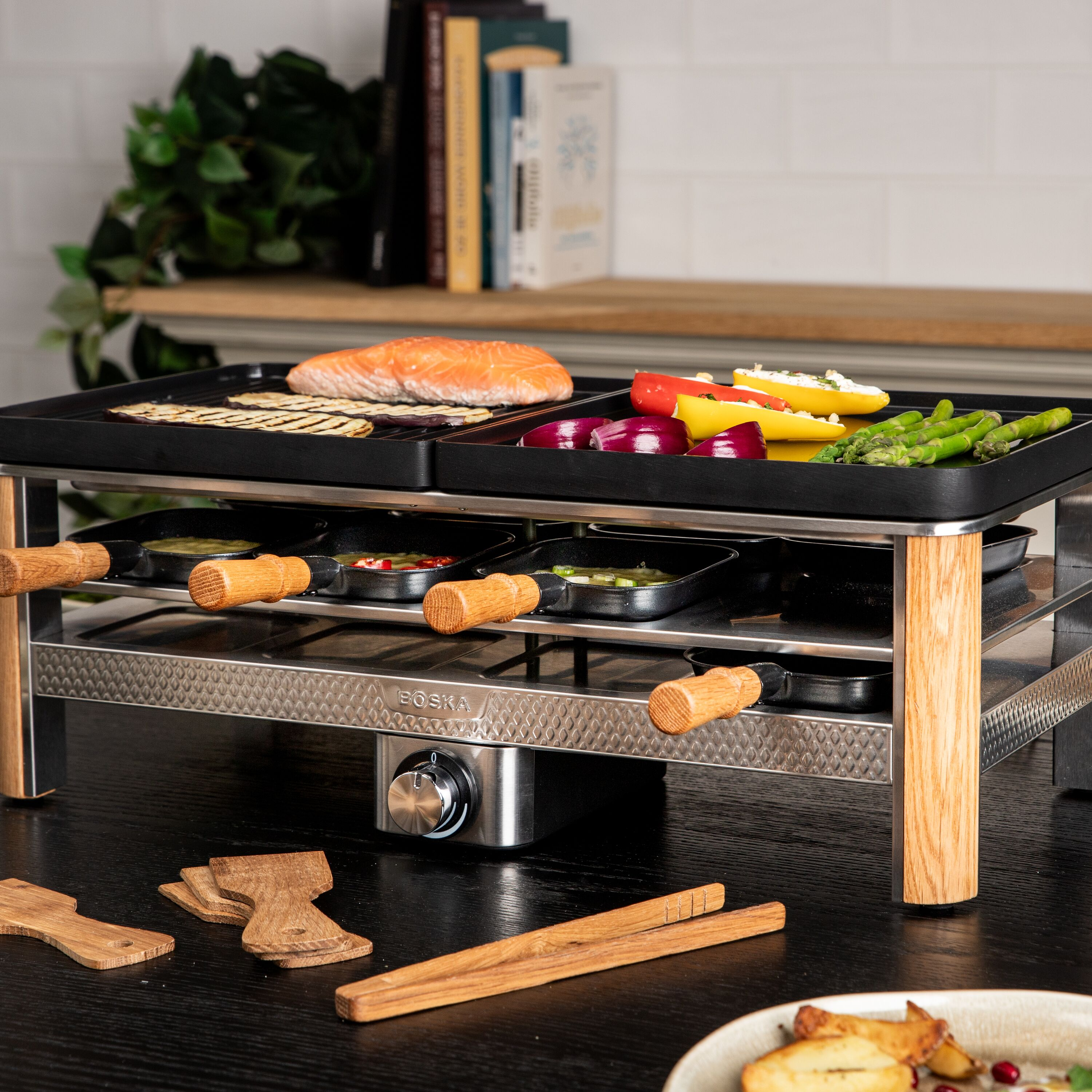 Ein elektrischer Tischgrill mit Lachs und Gemüse auf der Grillplatte und kleinen Pfännchen darunter.