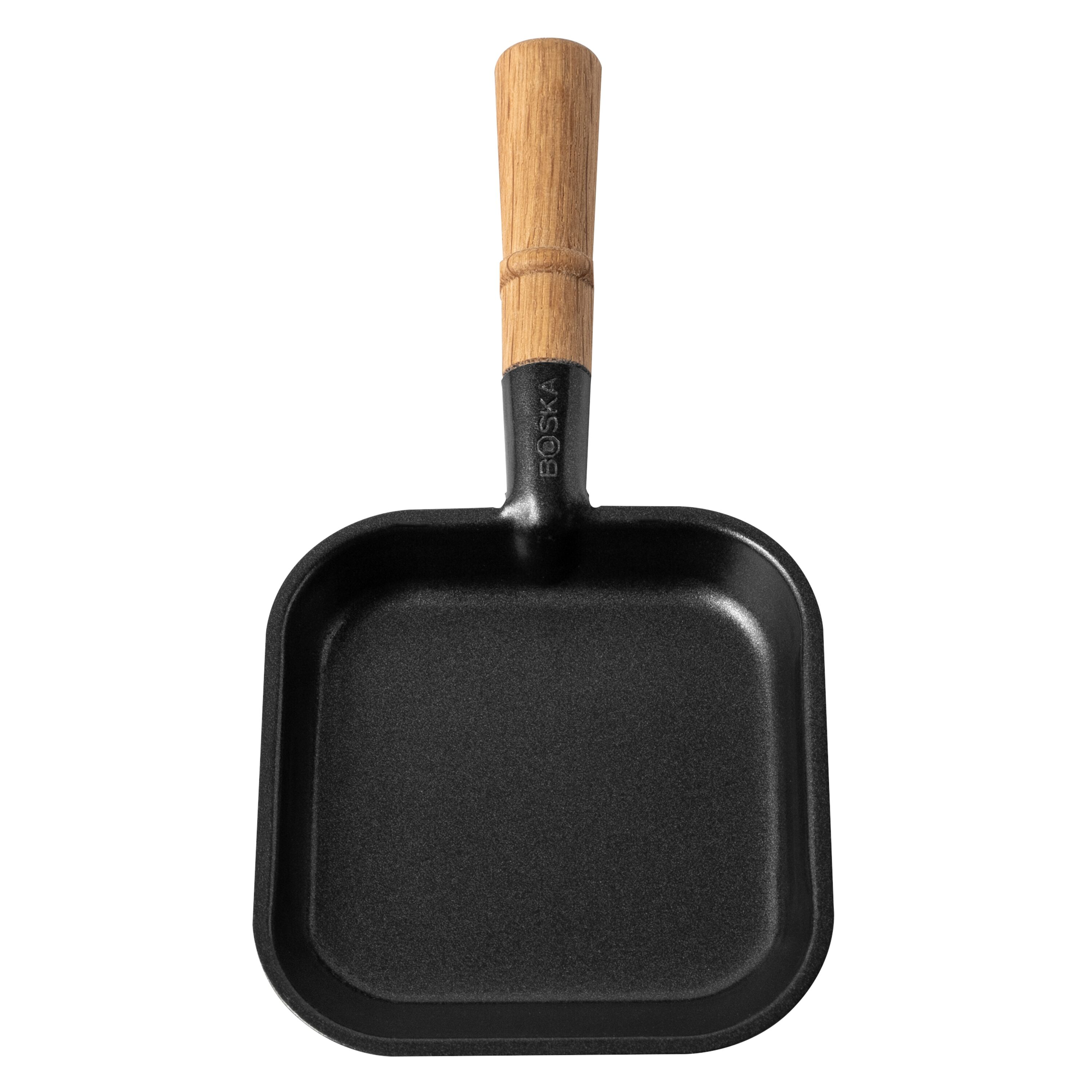 Eine kleine schwarze quadratische Pfanne mit einem langen Holzgriff auf weißem Hintergrund.