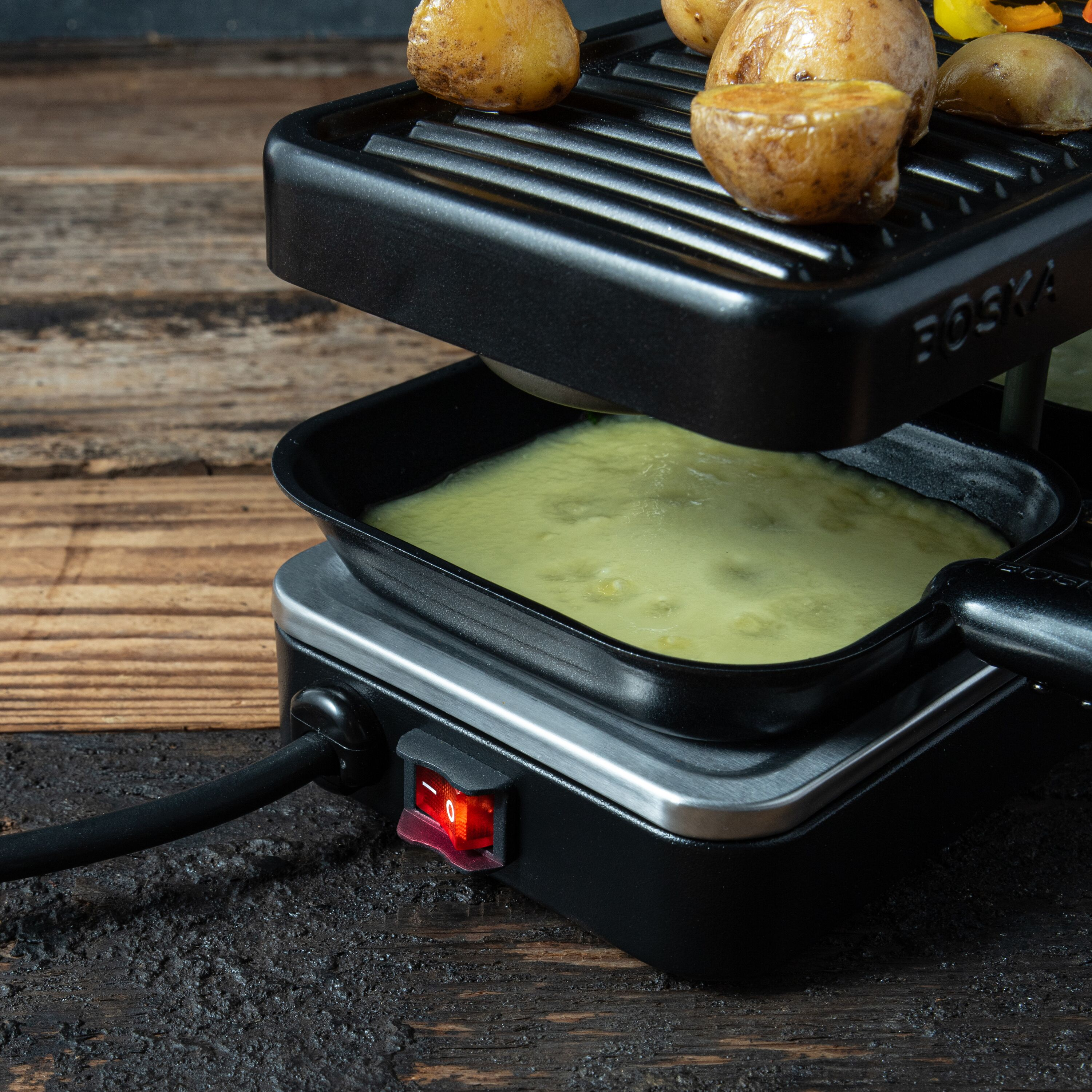 Raclette-Grill auf Holz Tisch mit geschmolzenem Käse und Kartoffeln.