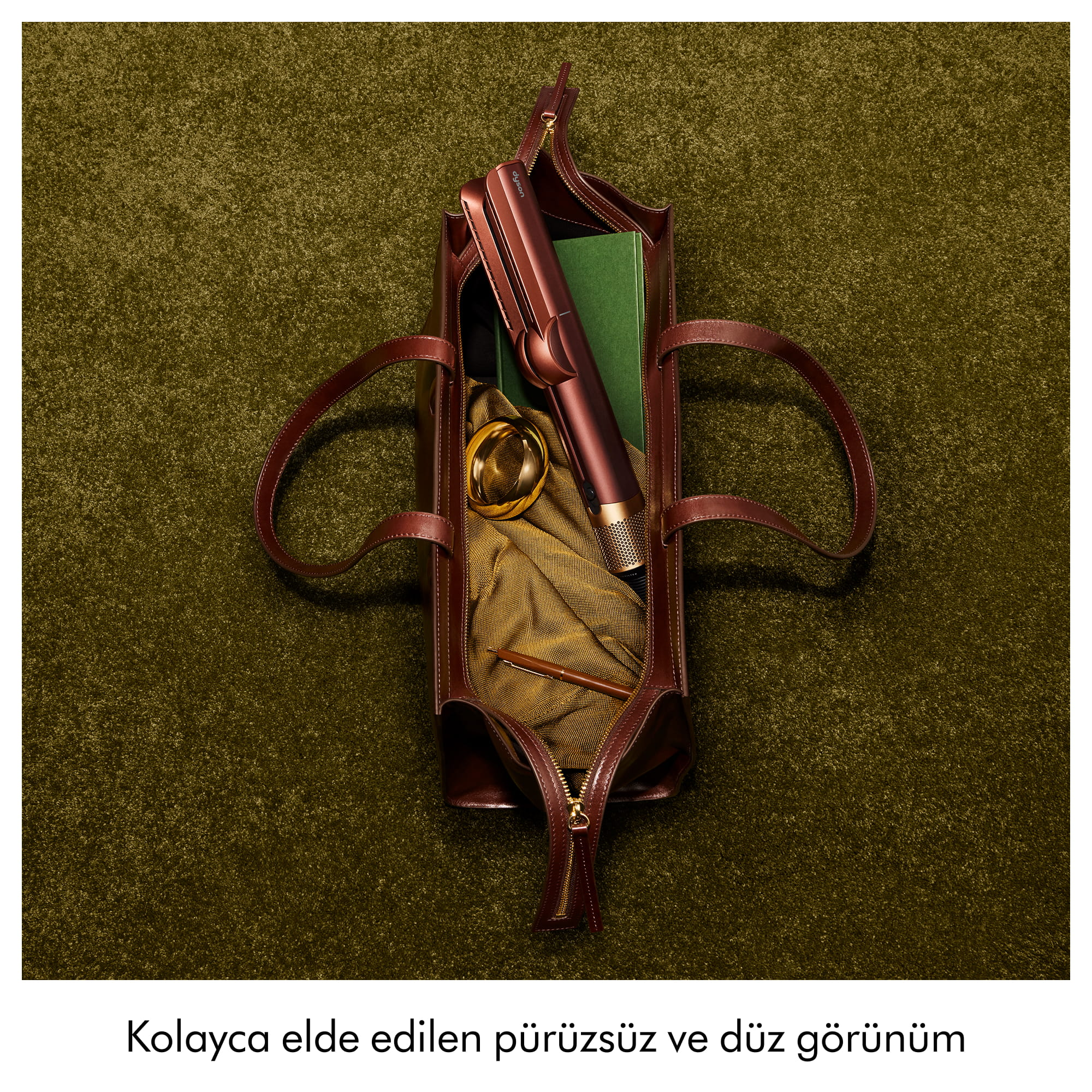 Yesil hali uzerinde kahverengi deri canta, icinde sac sekillendirici, kitap, kumas.