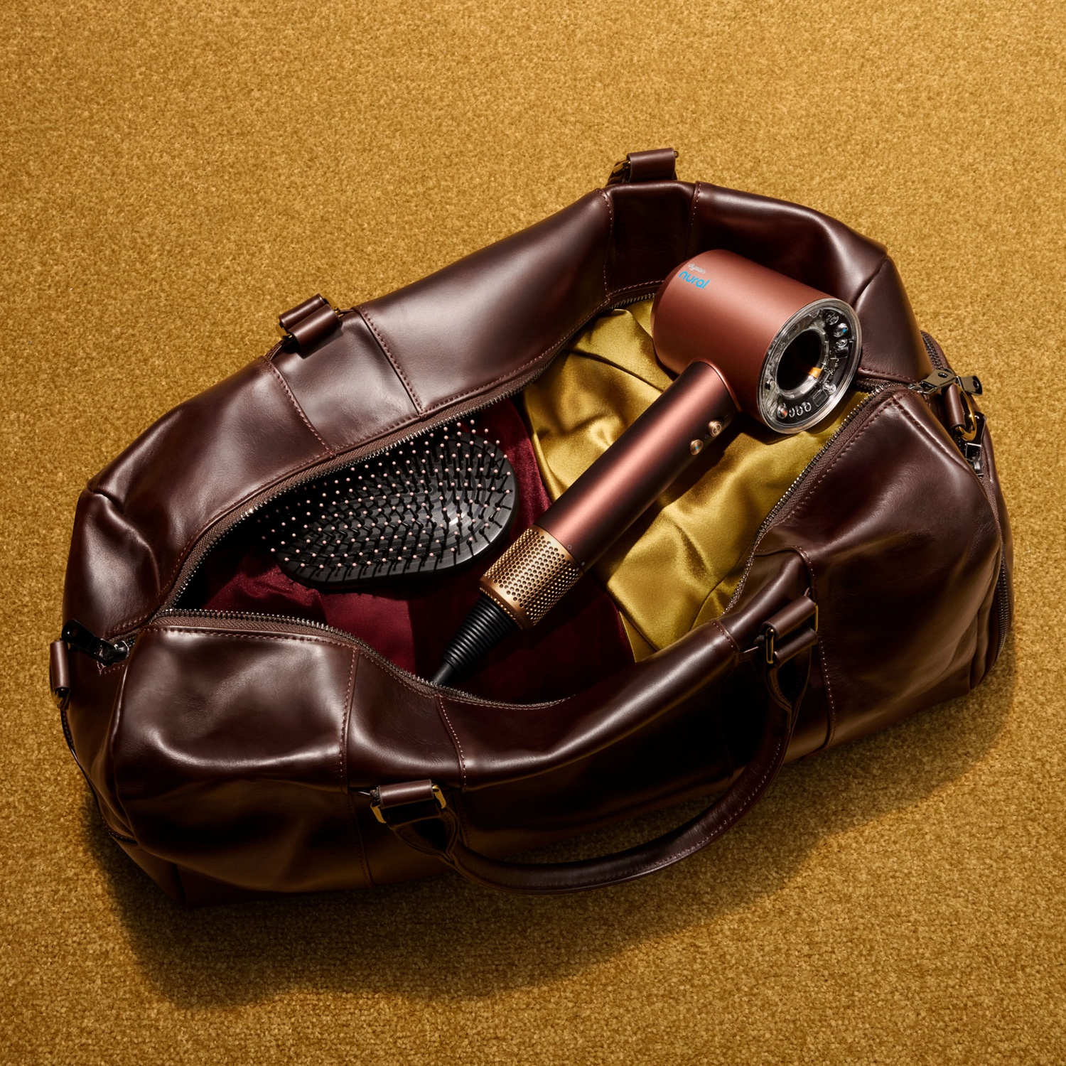 Brown leather bag on yellow carpet containing a hairdryer, brush, and fabrics.