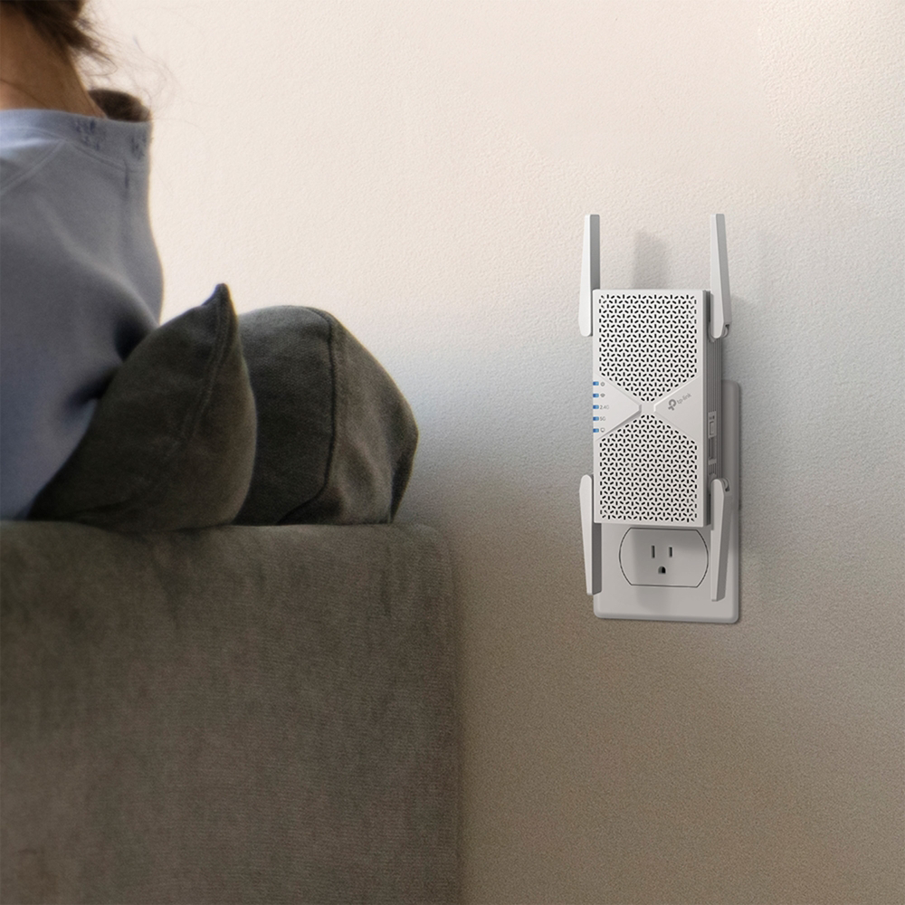 Egy fehér Wi-Fi jelerősítő van bedugva a fali aljzatba egy kanapé mellett.