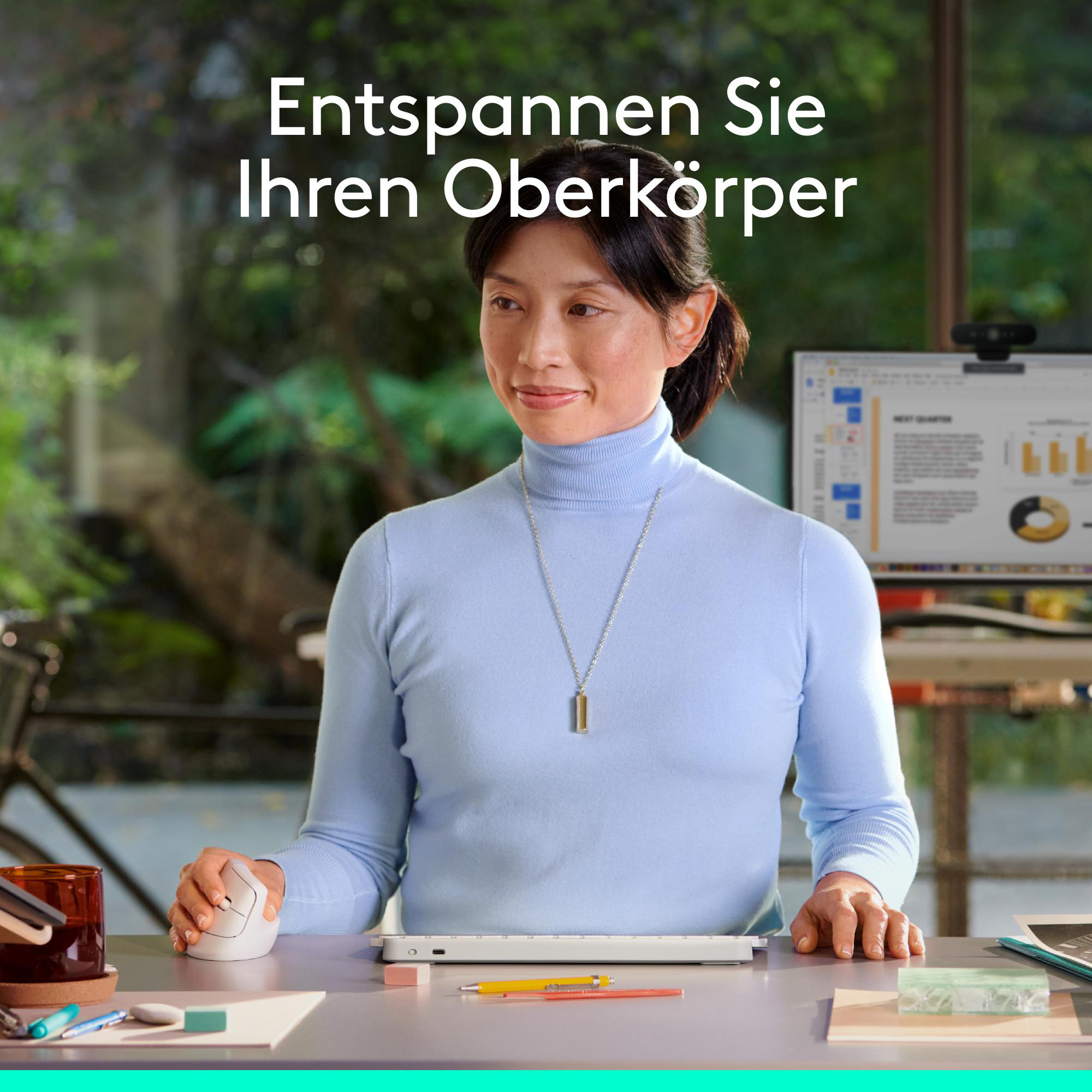 Eine Frau in blauem Rollkragenpullover sitzt am Schreibtisch vor einem Computer und benutzt eine weiße Computermaus.