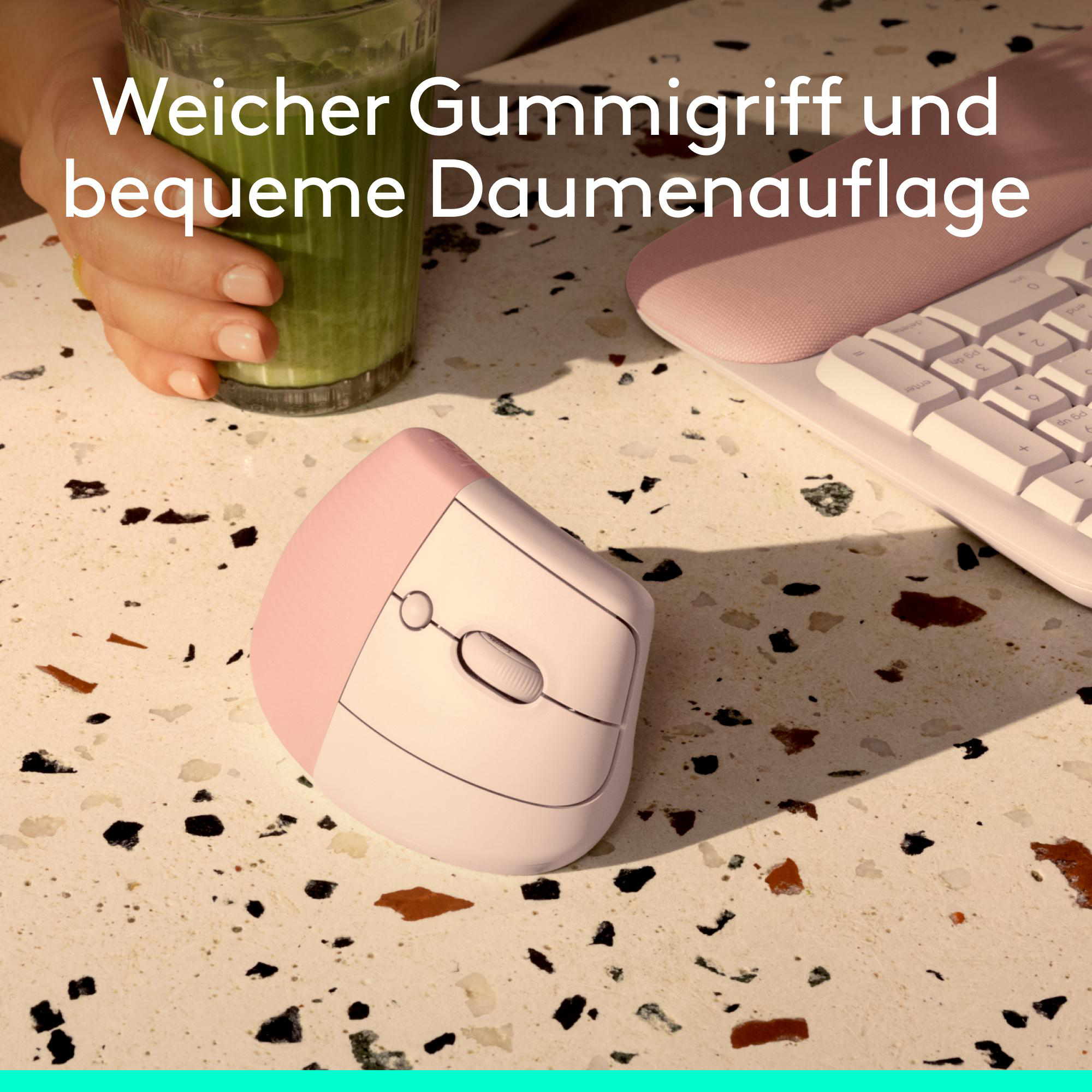 Eine pinke ergonomische Maus, eine Tastatur und ein grüner Smoothie auf einem terrazzoartigen Tisch.