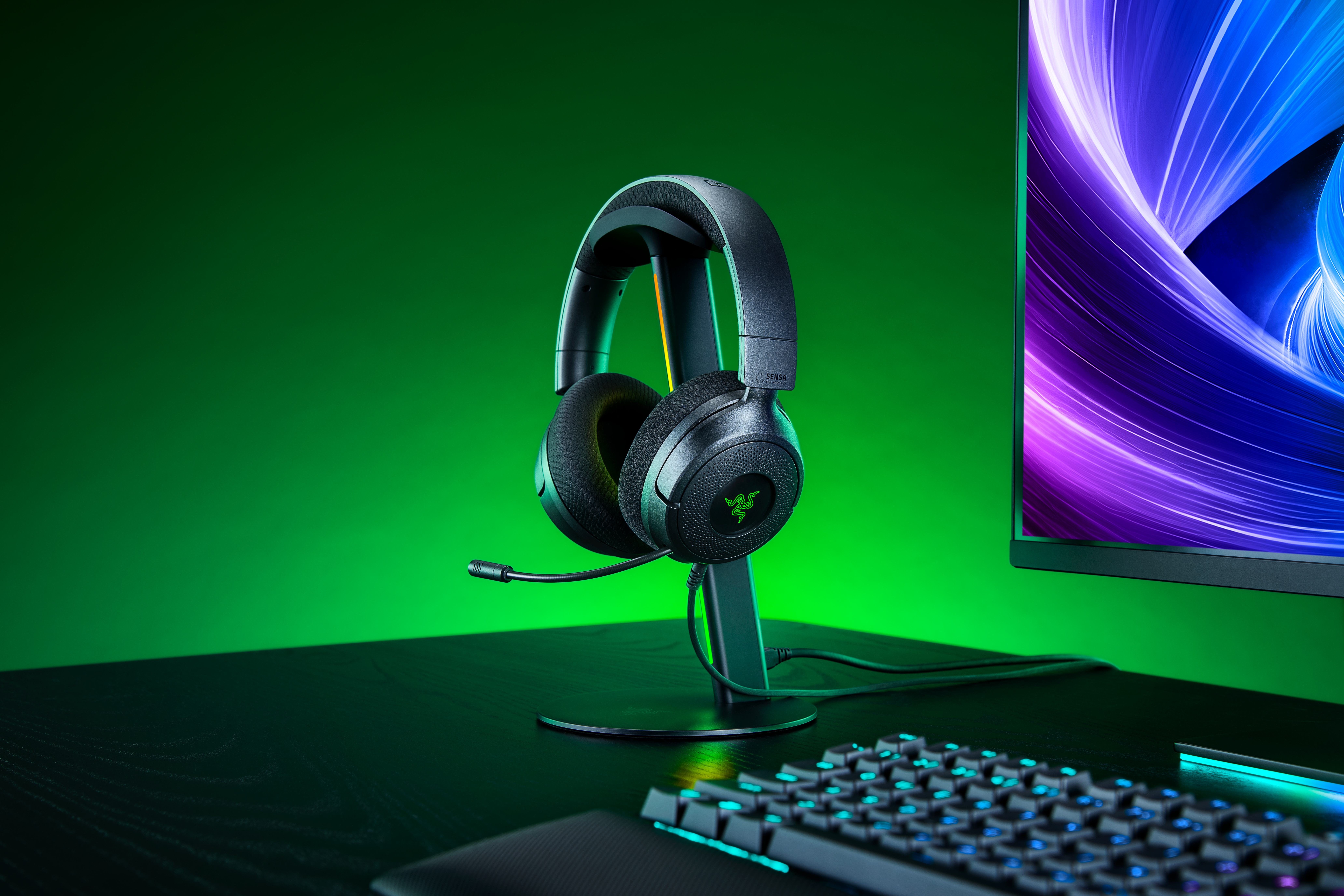 Schwarzes Gaming-Headset mit Mikrofon auf Ständer, vor grünem Hintergrund mit Monitor.