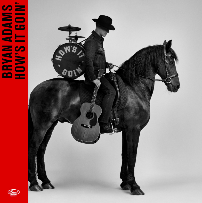 Ein Mann mit Hut sitzt auf einem schwarzen Pferd, hält eine Gitarre und hat eine Trommel auf dem Rücken.