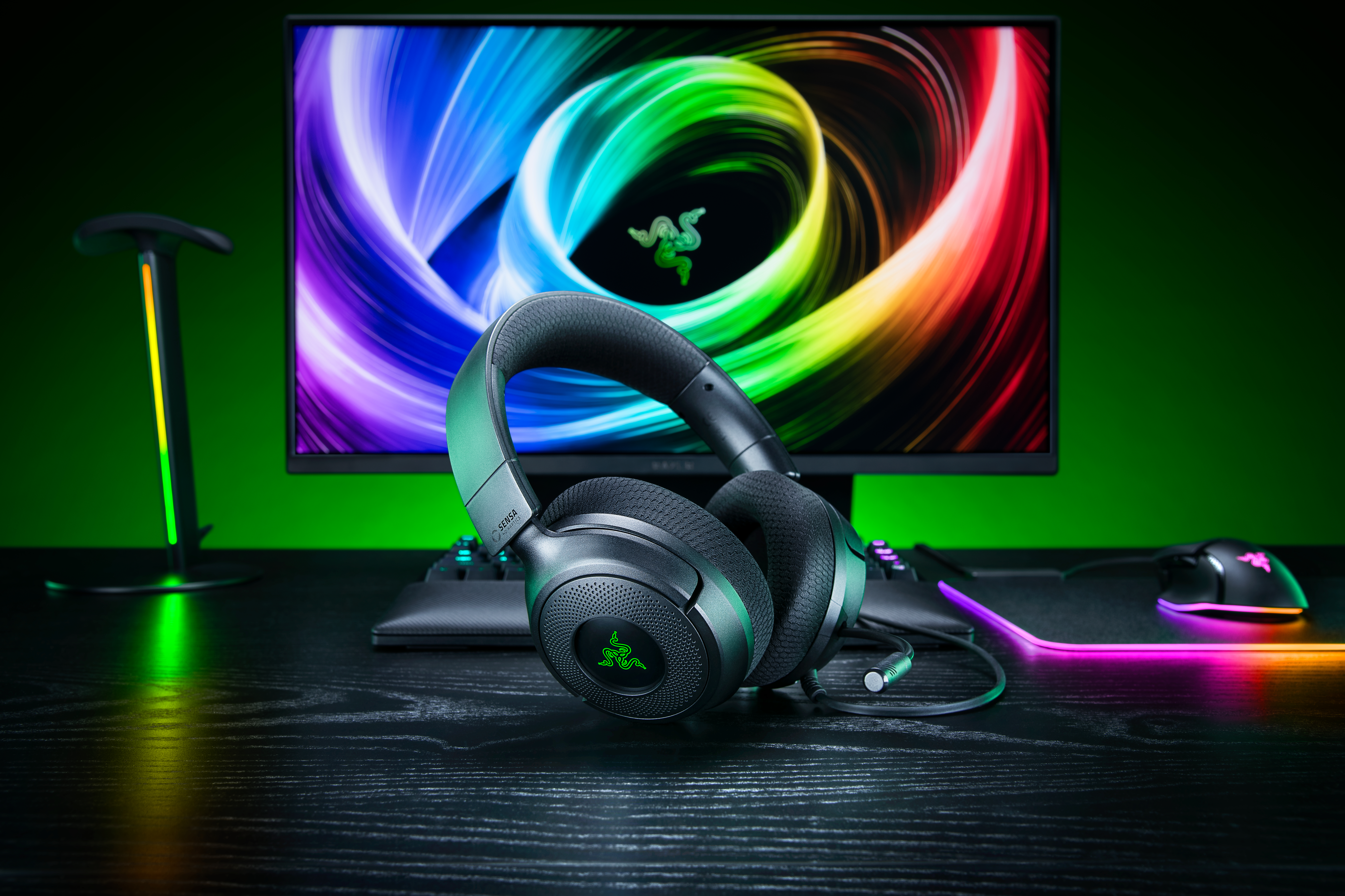Schwarzes Gaming-Headset auf einem Schreibtisch vor einem Monitor mit farbigem Wirbel-Hintergrund.