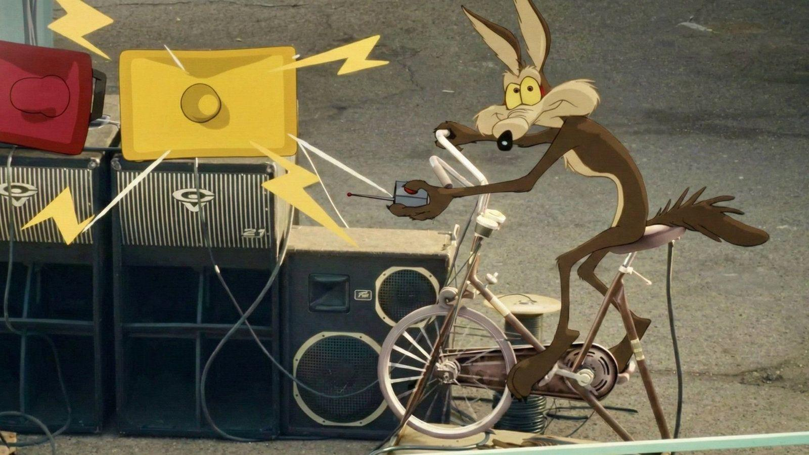 Wile E. Coyote sitzt auf einem Fahrrad vor großen Lautsprechern und hält eine Fernbedienung.