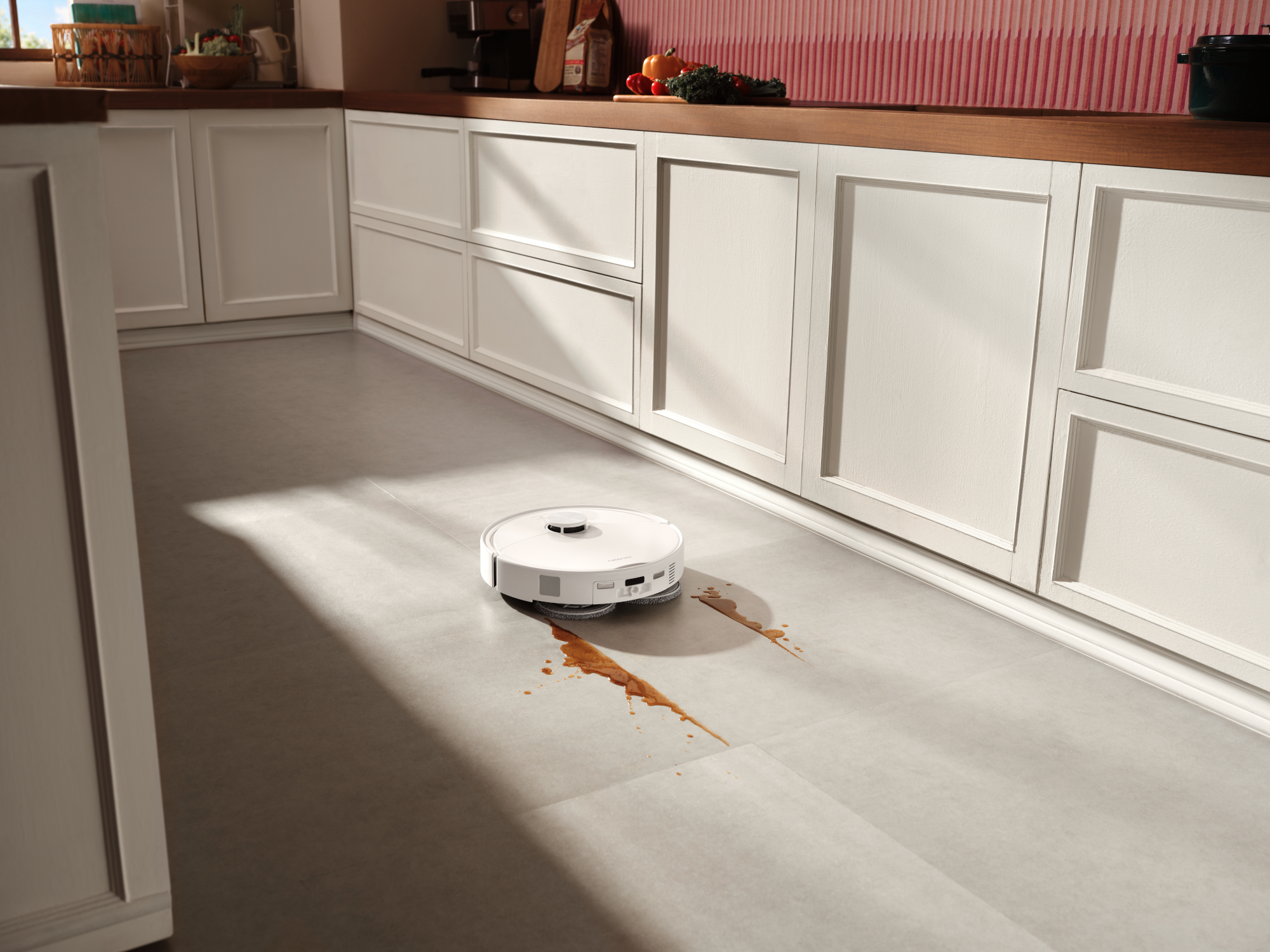 Egy fehér robotporszívó feltakarítja a kiömlött folyadékot egy világos konyha padlóján.