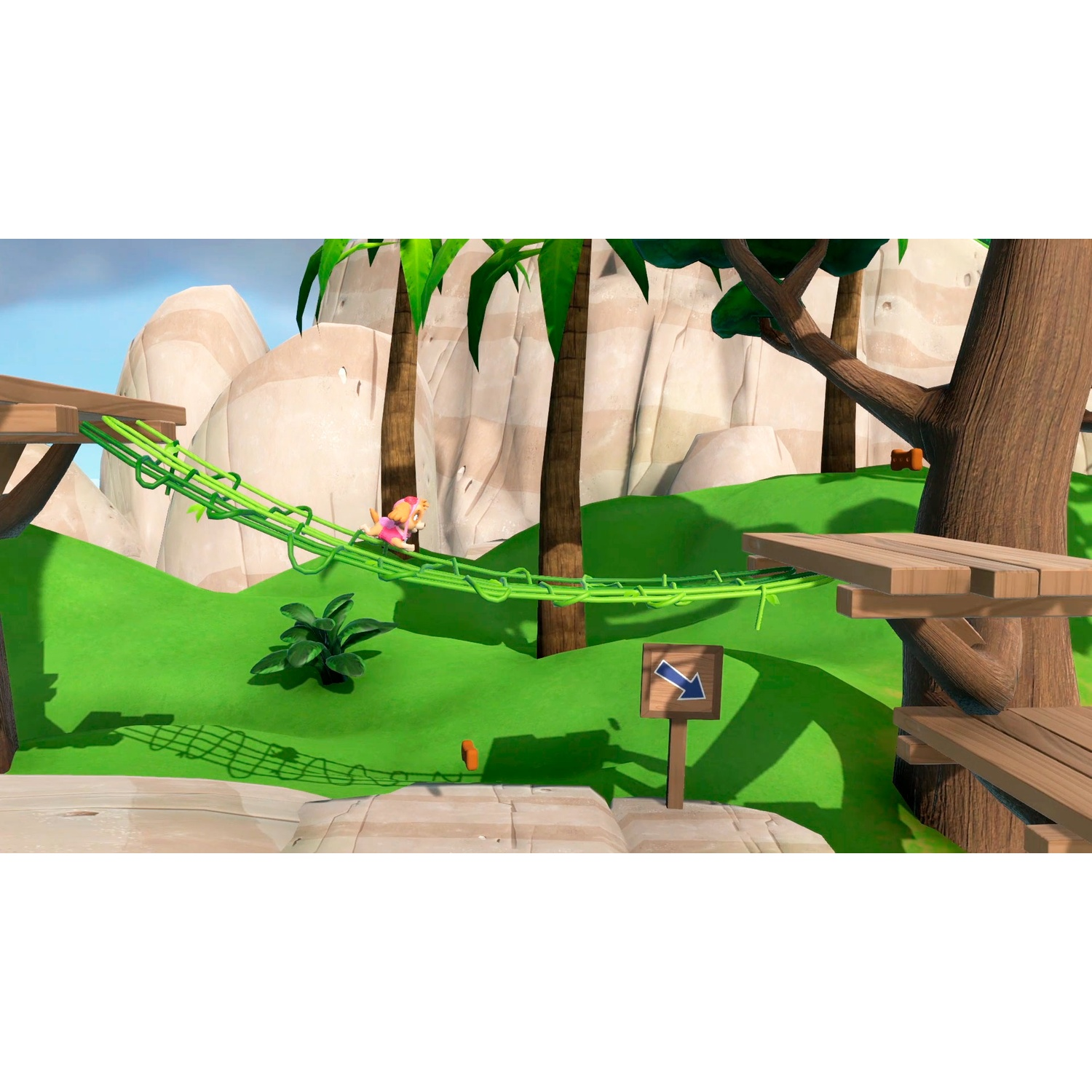 A small dog in pink clothing walks on a green rope bridge in a jungle landscape.