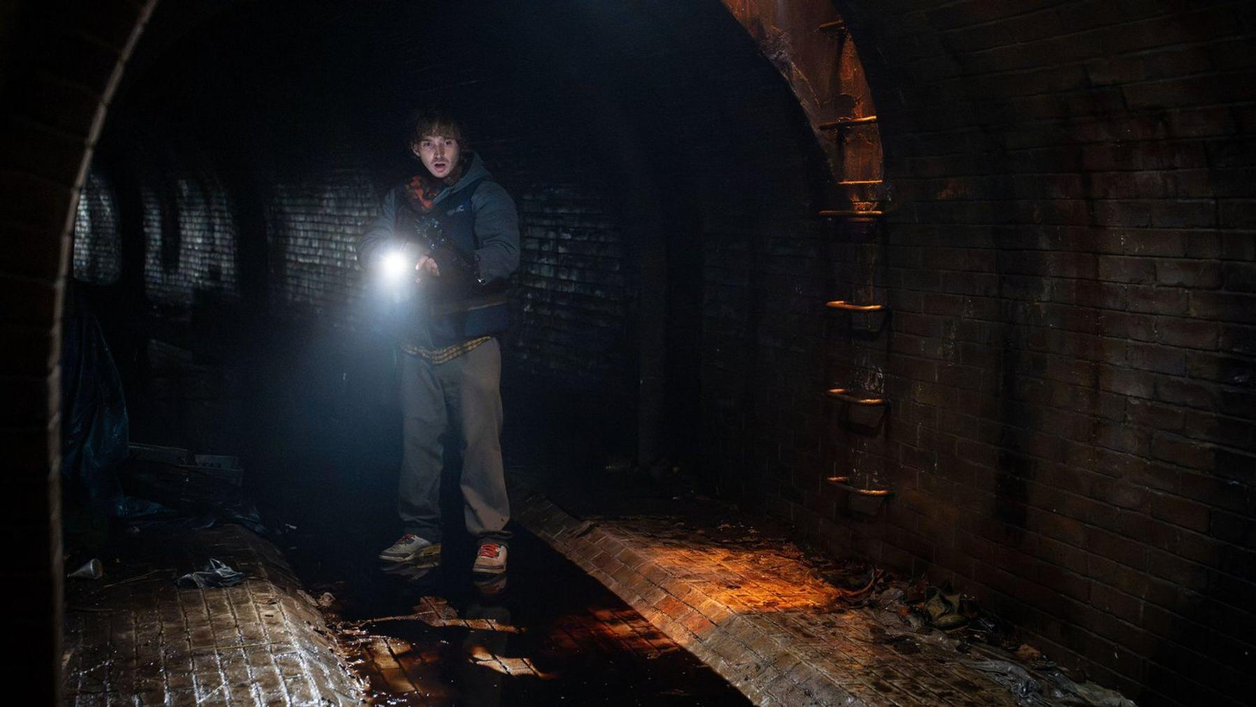 Ein junger Mann mit Taschenlampe steht im dunklen, gewölbten Backsteintunnel.