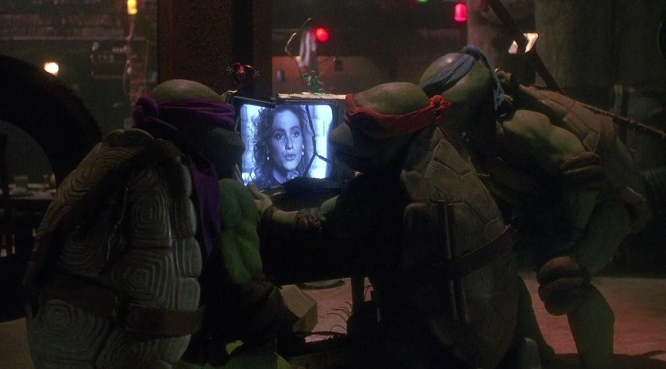 Drei Ninja Turtles schauen gemeinsam in einem dunklen Raum auf einen kleinen, leuchtenden Fernseher.