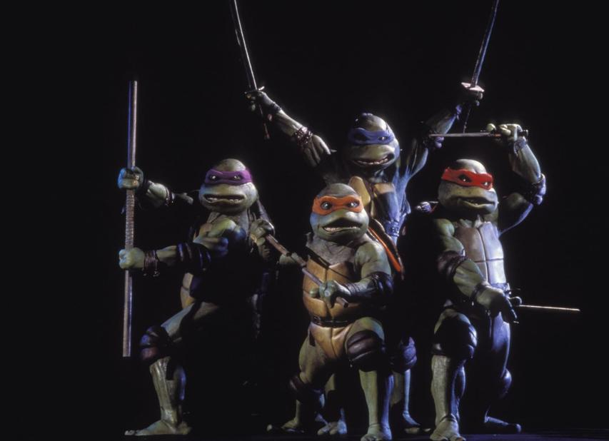 Vier Teenage Mutant Ninja Turtles posieren mit ihren Waffen vor dunklem Hintergrund.