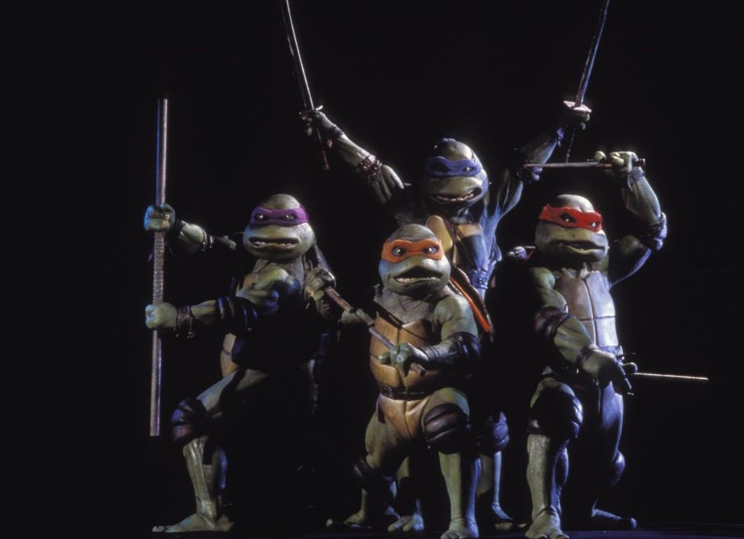 Vier Teenage Mutant Ninja Turtles posieren mit Waffen vor schwarzem Hintergrund.