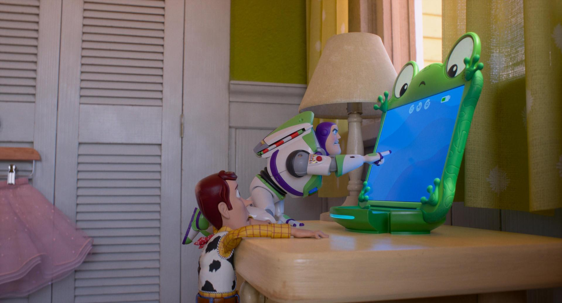 Woody und Buzz Lightyear betrachten gemeinsam einen Frosch-Computer auf einem Holztisch.