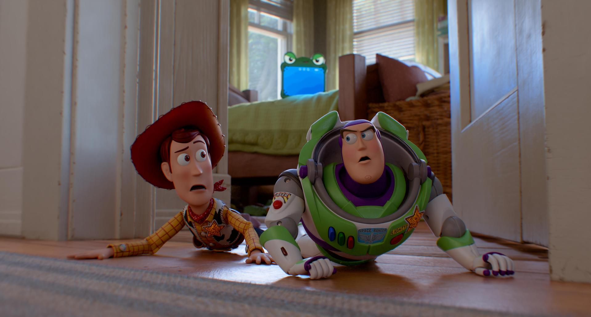 Woody und Buzz Lightyear wirken schockiert, während sie auf einem Holzboden in einem Schlafzimmer kriechen.