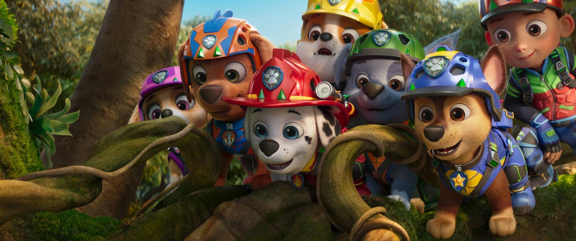 Ryder und die Welpen der Paw Patrol in Helmen hinter grünen Ranken im Wald.
