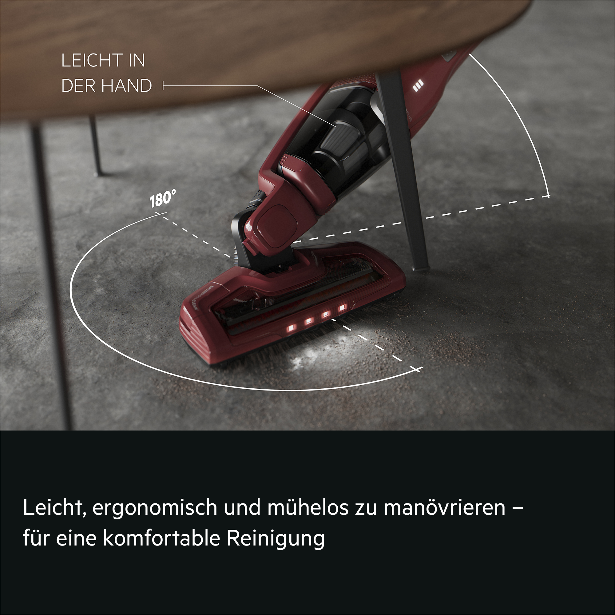 Roter kabelloser Staubsauger reinigt unter einem Holztisch mit 180 Grad Schwenkradius.