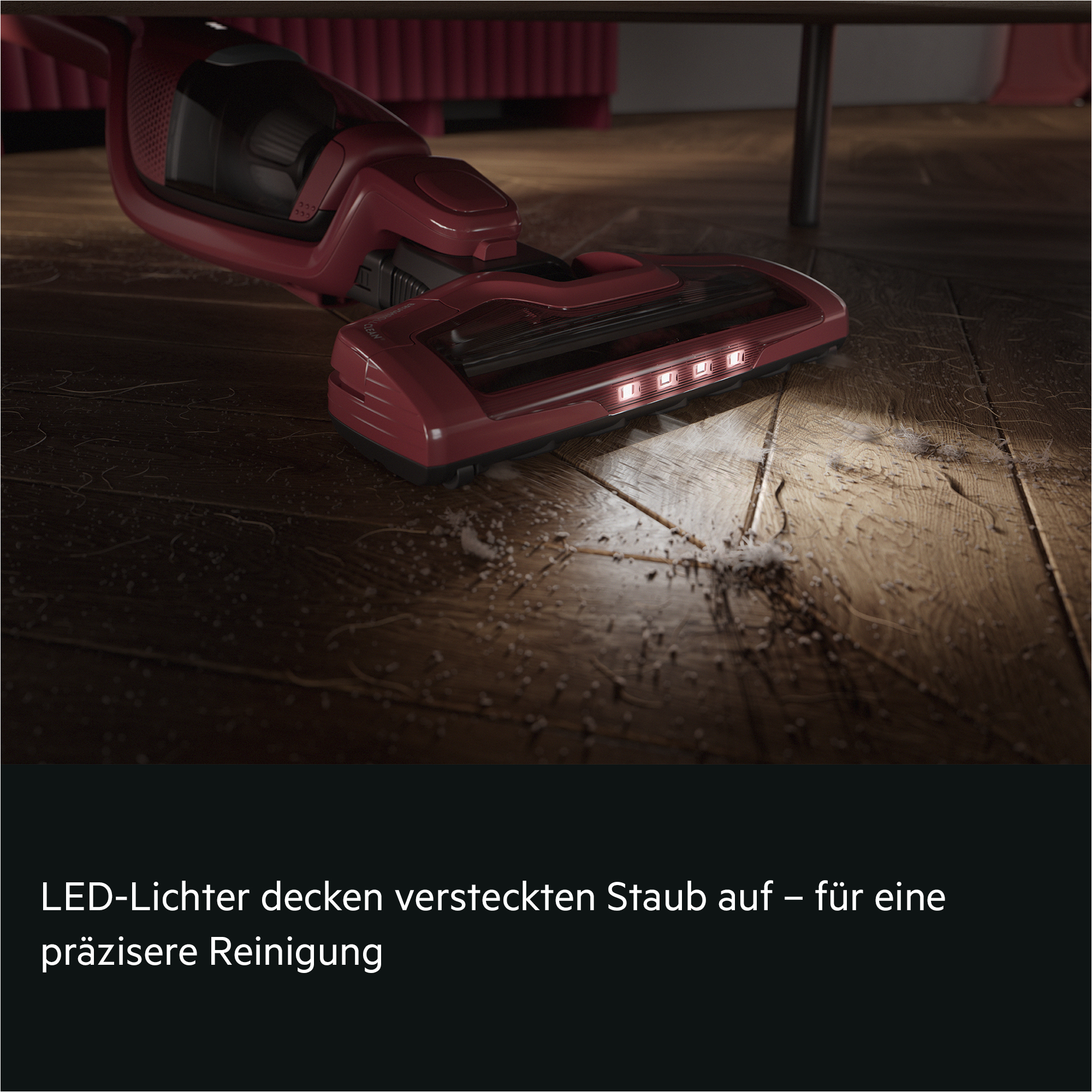 Ein roter Staubsauger mit LED-Lichtern reinigt einen Holzfußboden unter Möbeln.