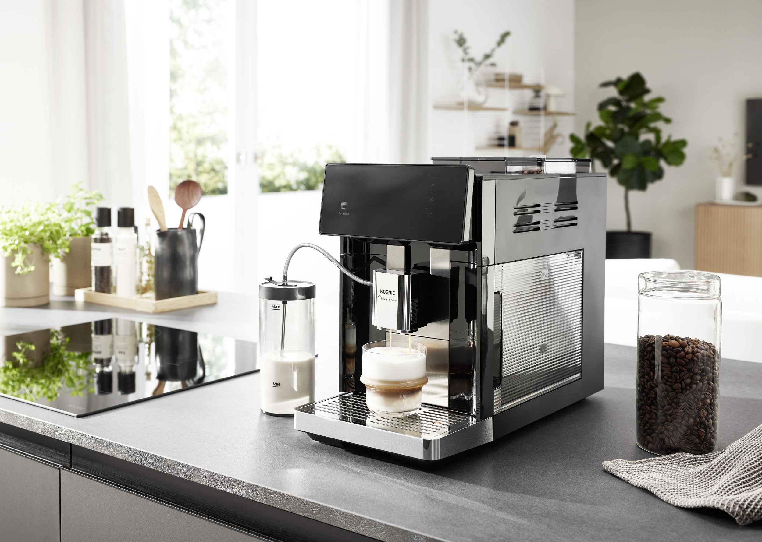 Eine schwarze Kaffeemaschine brüht Kaffee in ein Milchglas auf einer Küchentheke neben einem Milchbehälter und Kaffeebohnen.