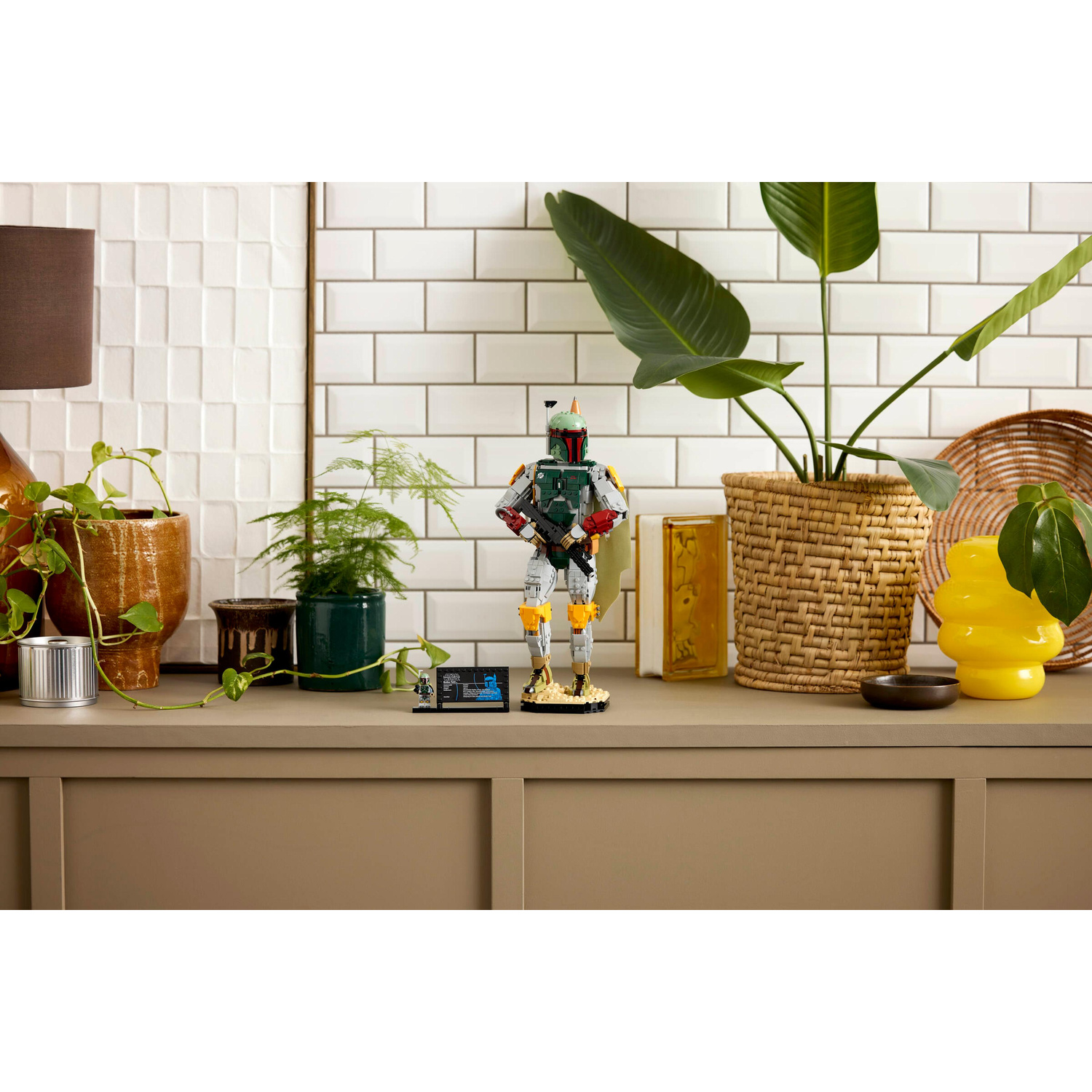 Figura Lego Boba Fett su mensola con piante e parete piastrellata sullo sfondo.