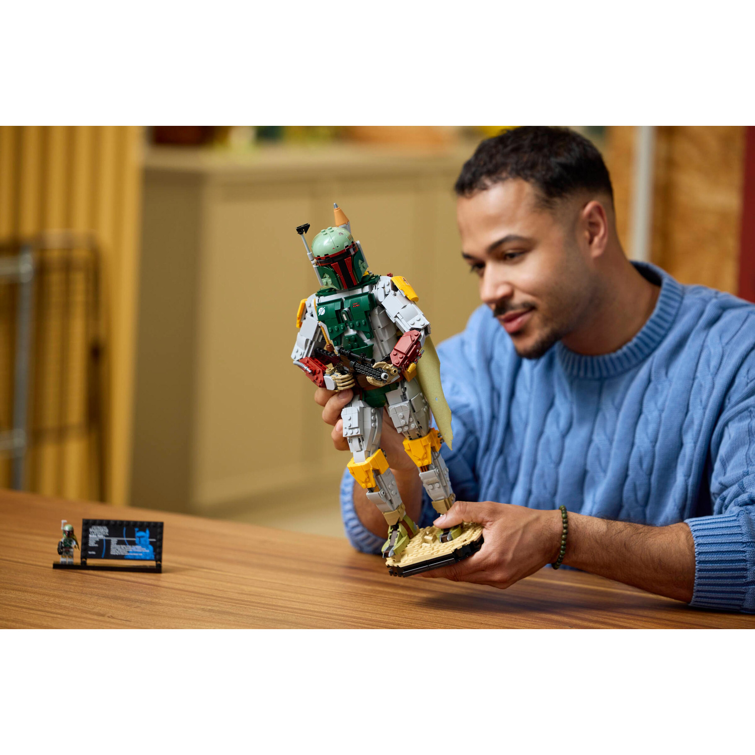 Un uomo in maglione blu tiene in mano una grande statuetta Lego di Boba Fett.