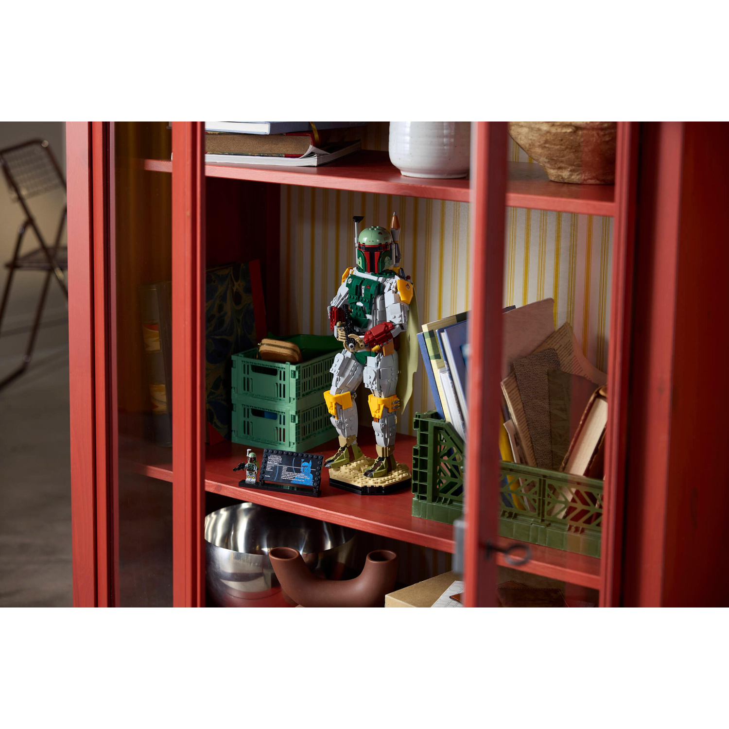 Una statuetta Lego di Boba Fett si trova in un mobile rosso tra libri e cestini.
